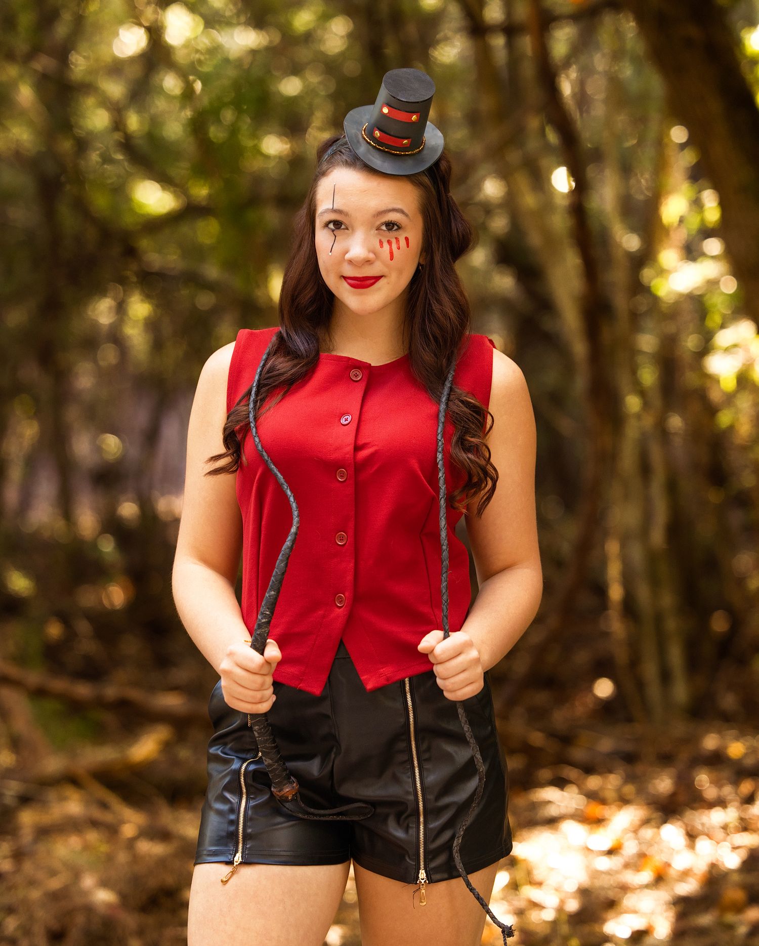 A festive outfit featuring a red sleeveless top, black shorts, and a tiny decorative top hat in a sunlit forest setting.