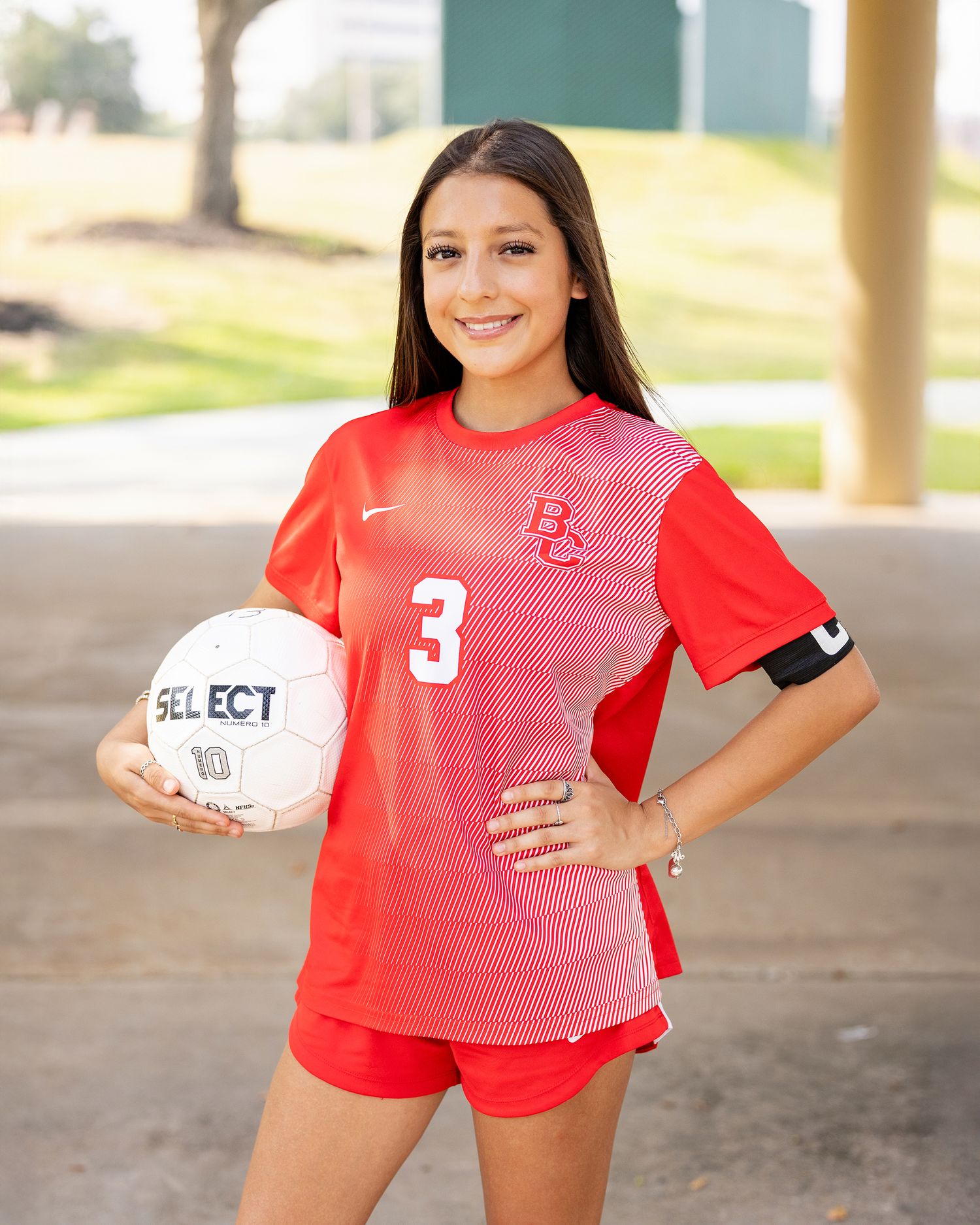 Volleyball player in red jersey poses with ball during outdoor sports photoshoot.