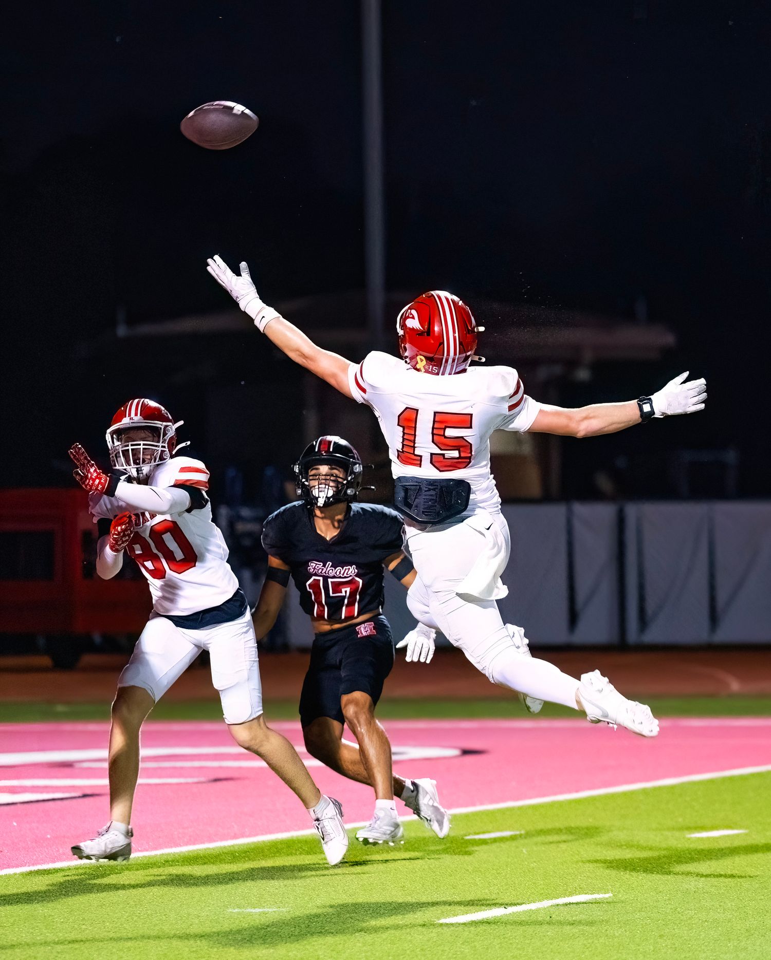 Football players dive and stretch to catch a pass during an intense game play.