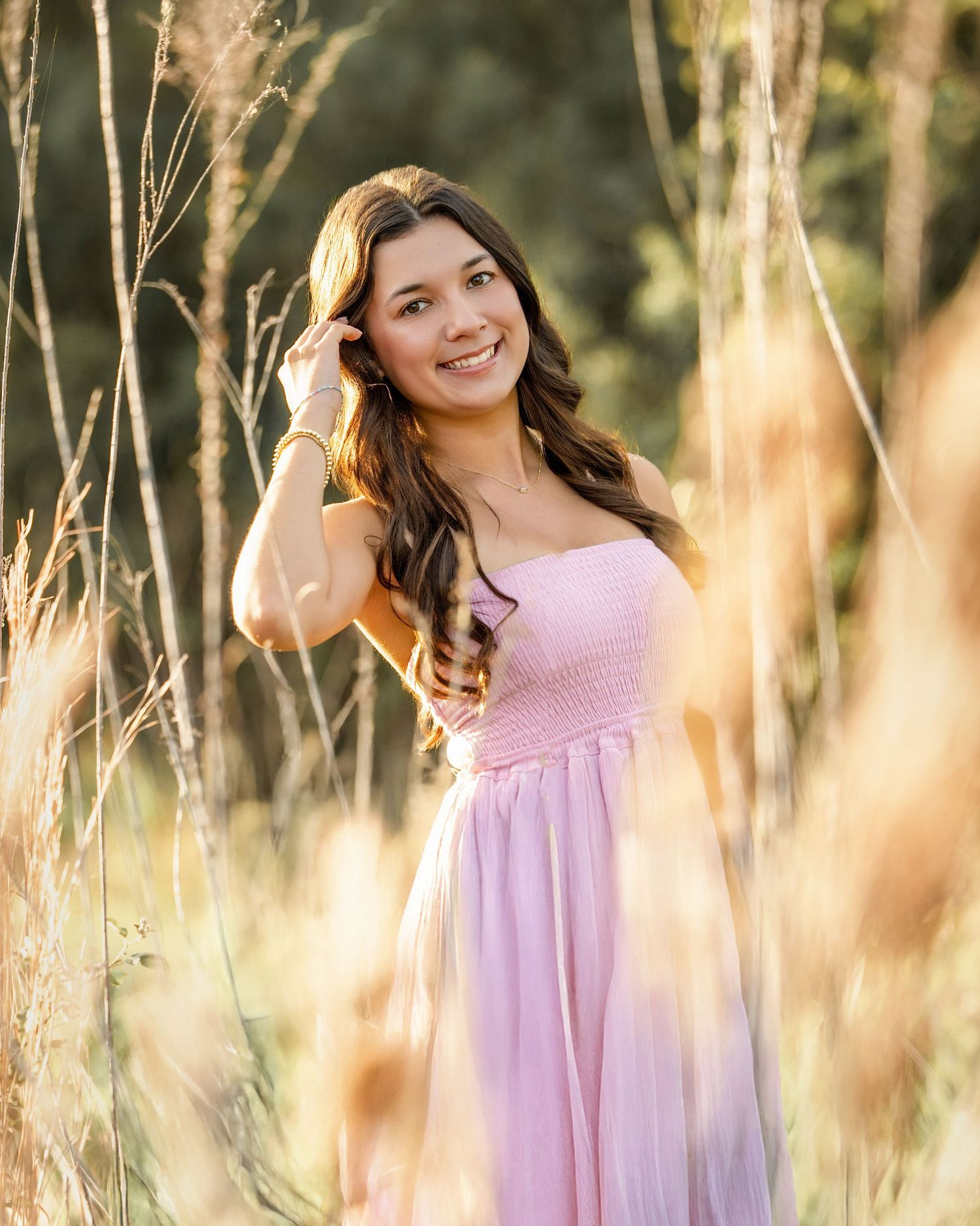 Young woman in pink strapless dress posing gracefully among golden tall grasses in a sunlit outdoor field.