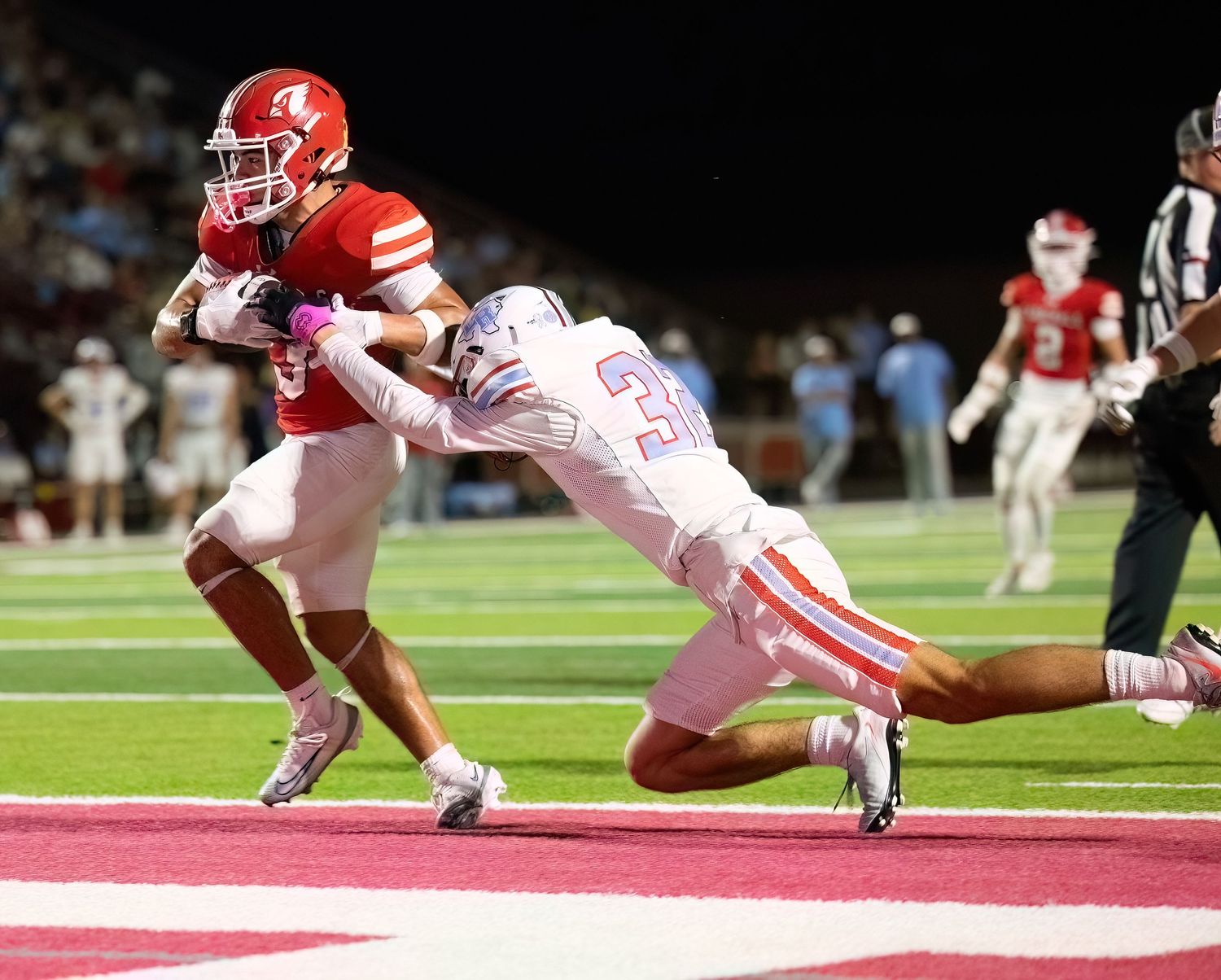 Football players dive and tackle during an intense game play on the field at night.
