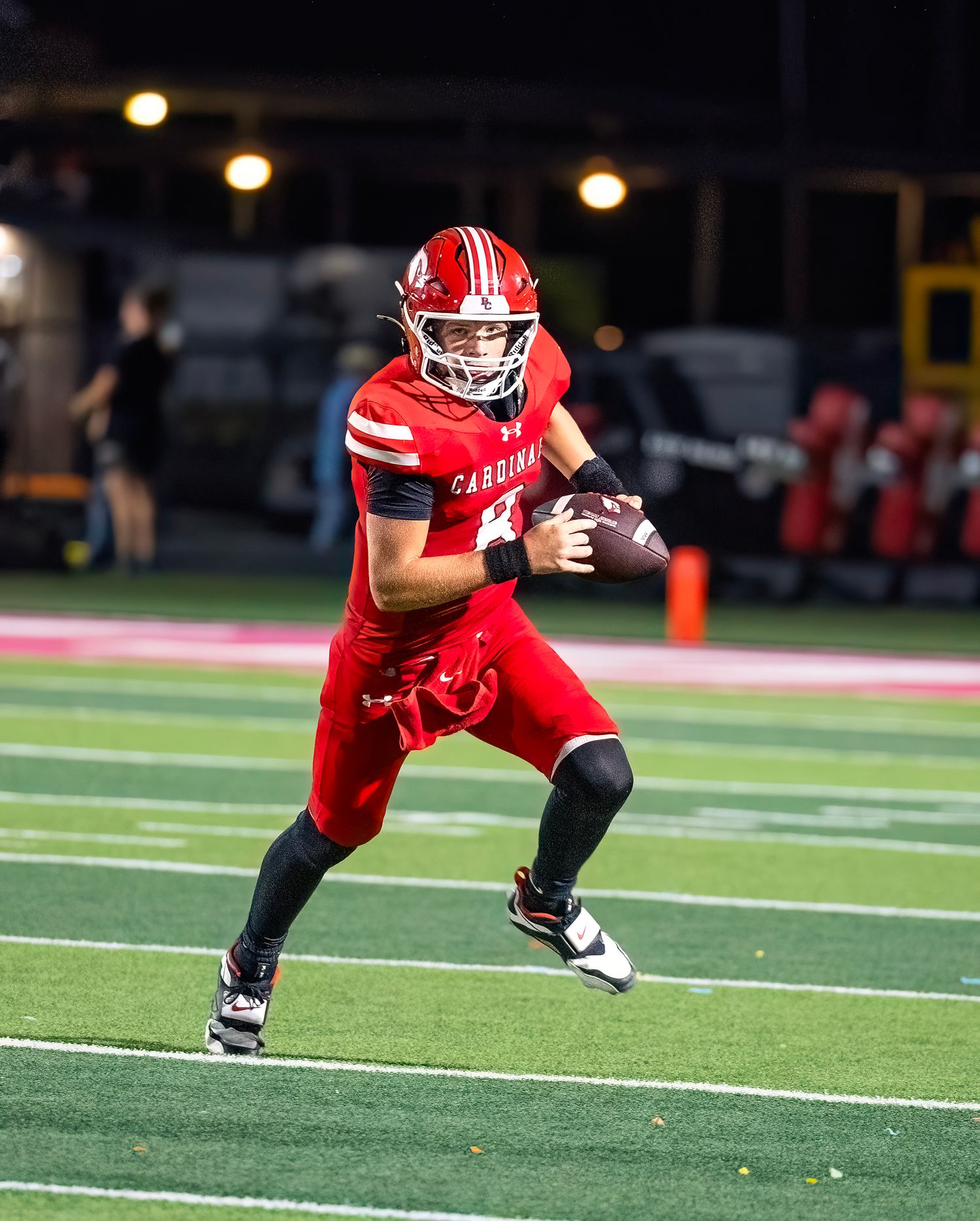 Football player in red uniform diving towards the goal line on a turf field during a night game.