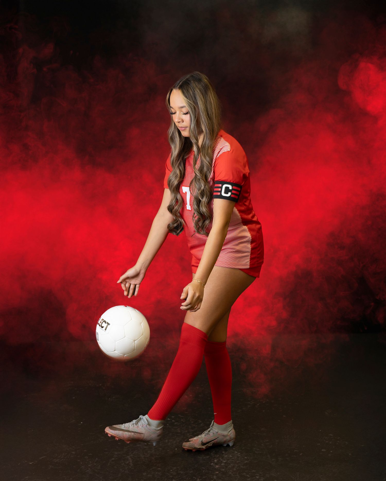 Volleyball player in red uniform poses dramatically with ball against dark background with red smoke effects.