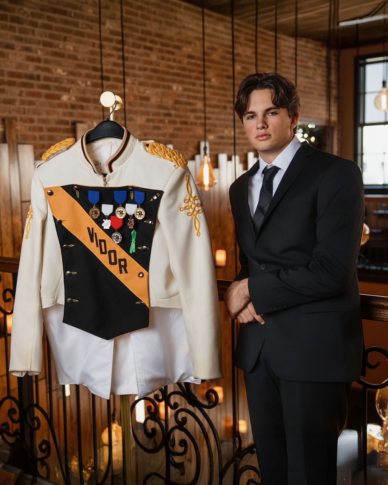 A decorated military uniform jacket on display next to a person wearing a black suit in a brick-walled room.