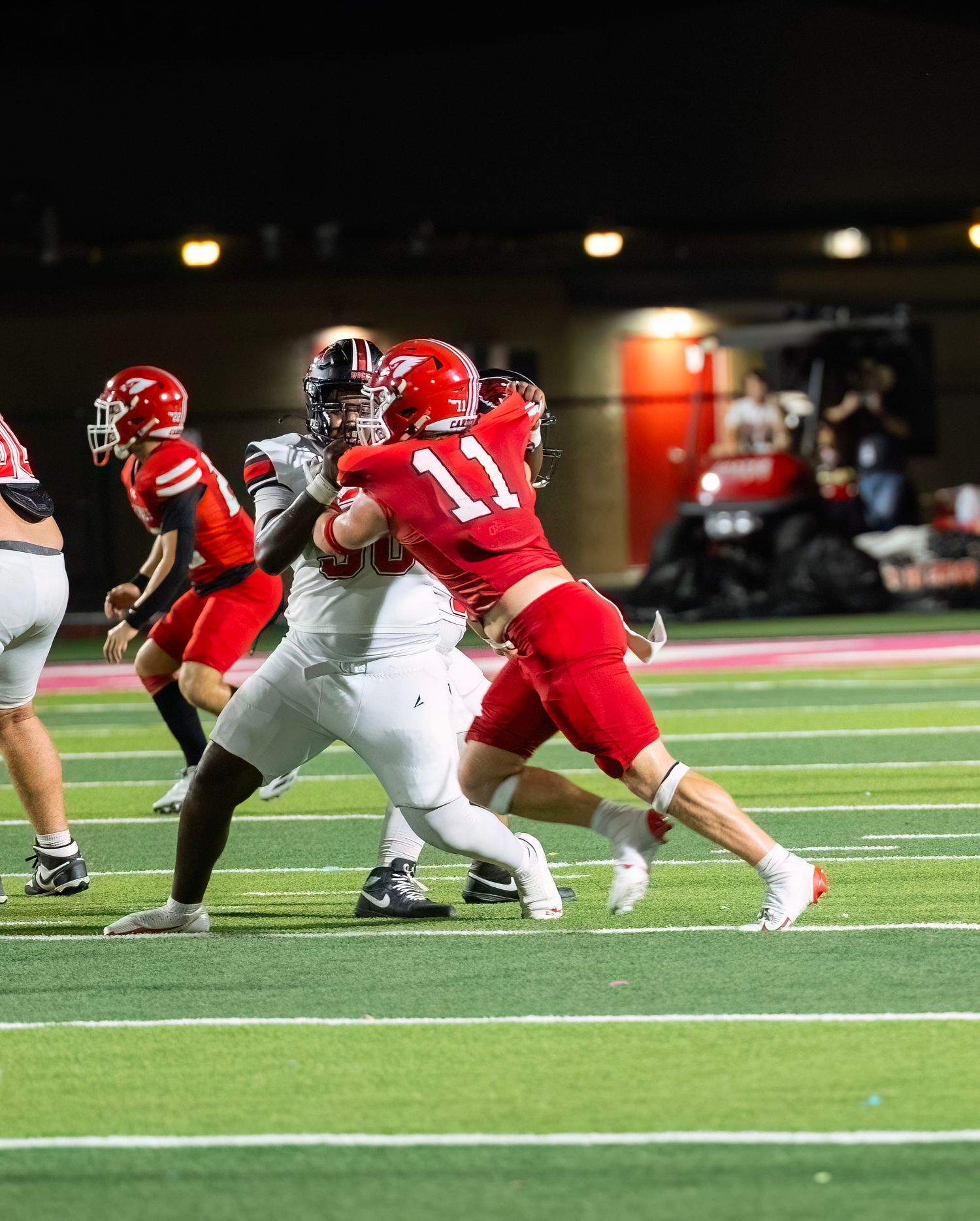 Football players in red and white uniforms clash during an intense defensive play on a nighttime field.