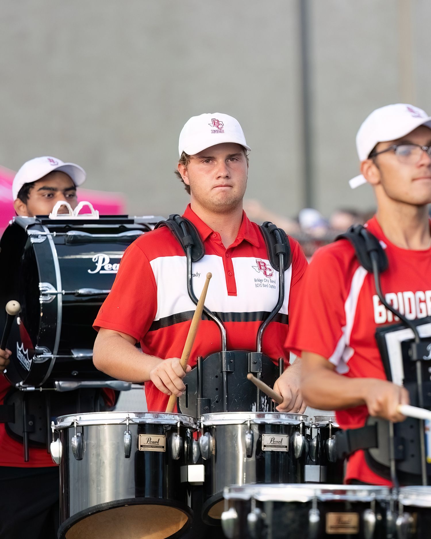 Members of a marching band drumline perform in red uniforms with white caps during an outdoor event.