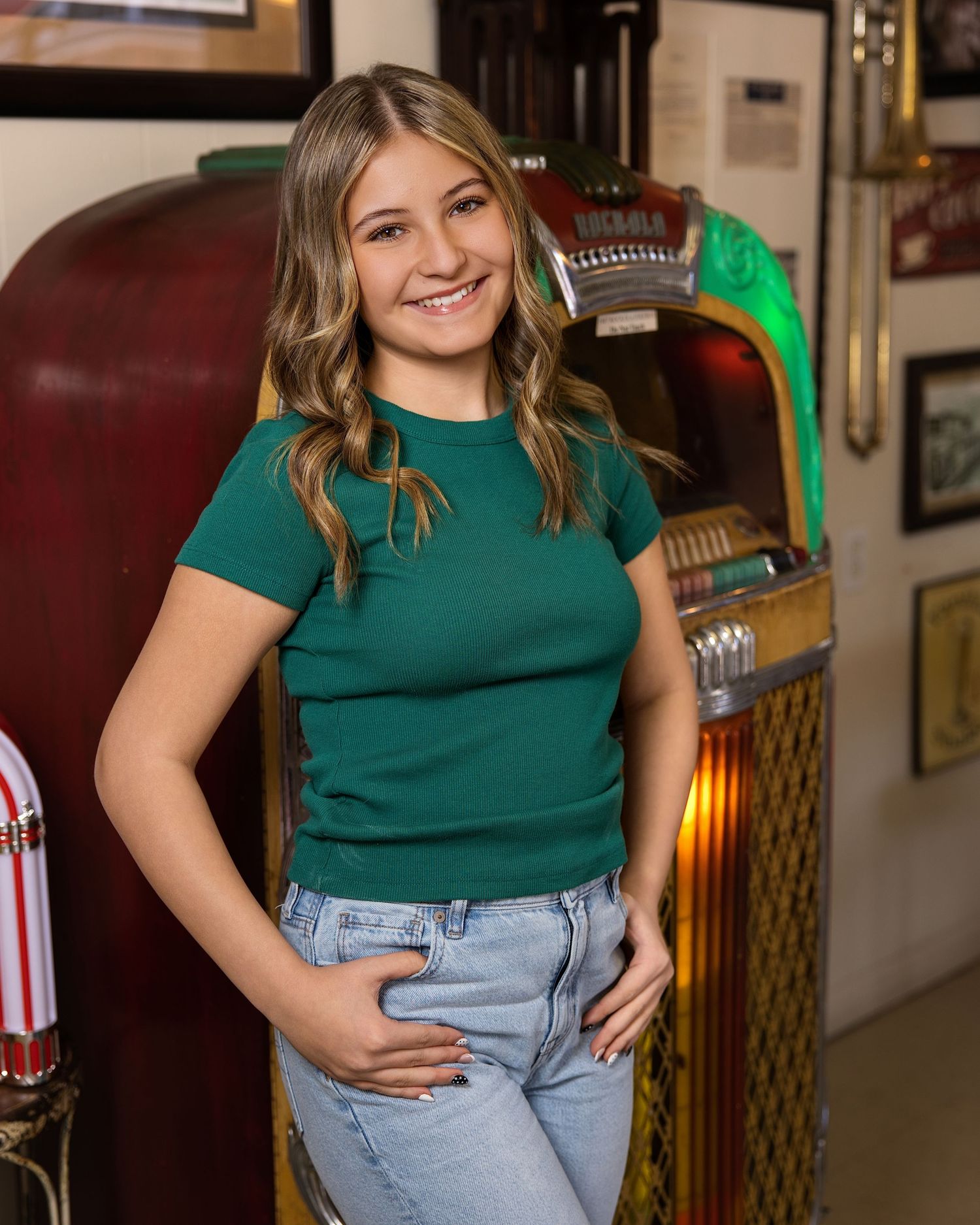A person wearing a green shirt and light jeans poses casually in a restaurant or bar setting.