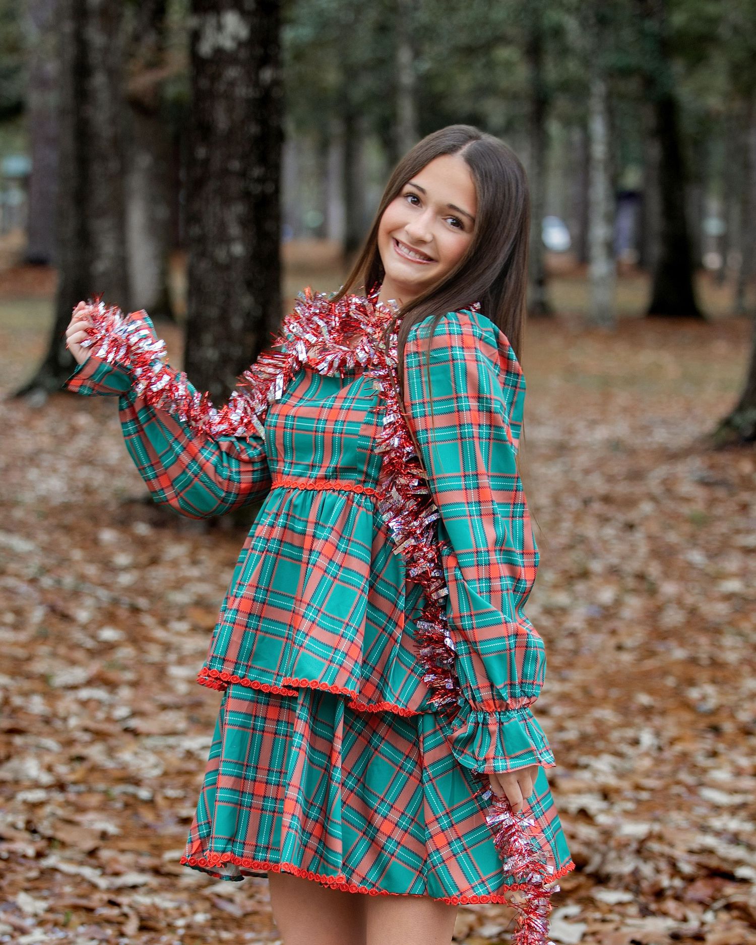 A festive plaid holiday outfit with ruffles is showcased against a backdrop of fallen autumn leaves.