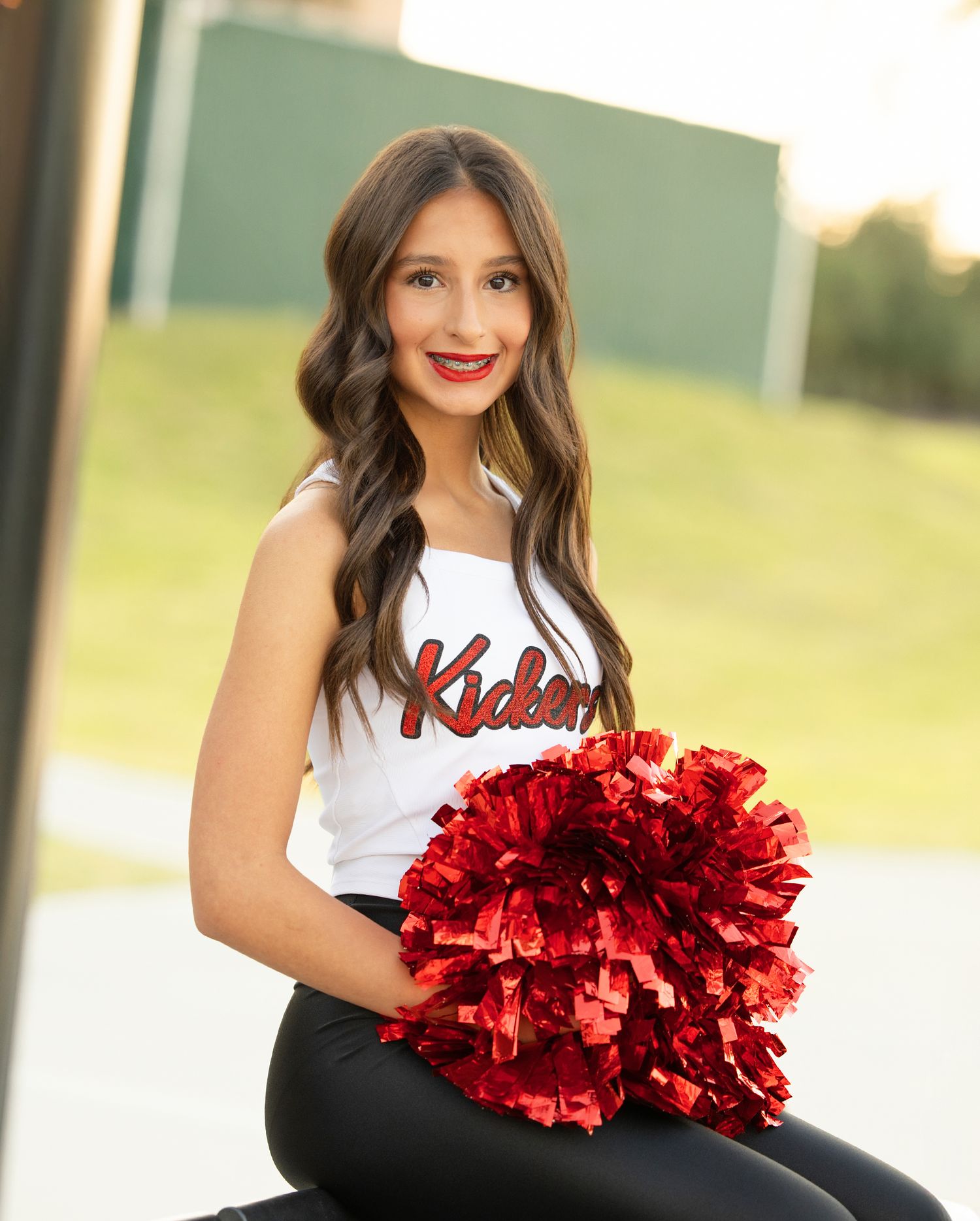 Cheerleader poses with red metallic pom poms in athletic uniform.
