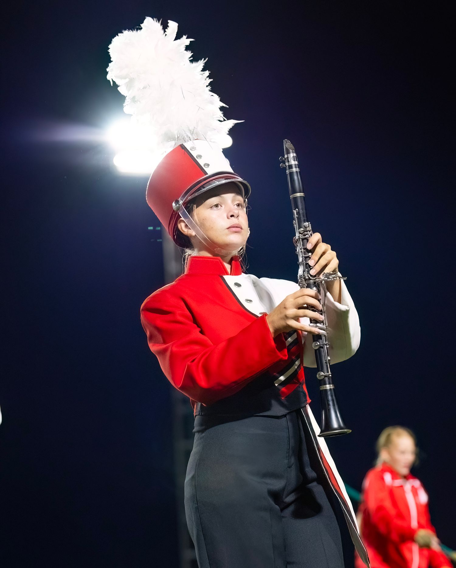 Bridge City High School Marching band members in red and black uniforms play instruments under stadium lights.