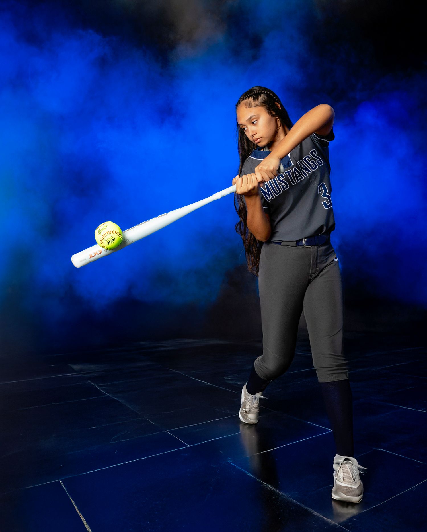 Softball player demonstrates batting stance progression against vibrant blue background during sports photoshoot.
