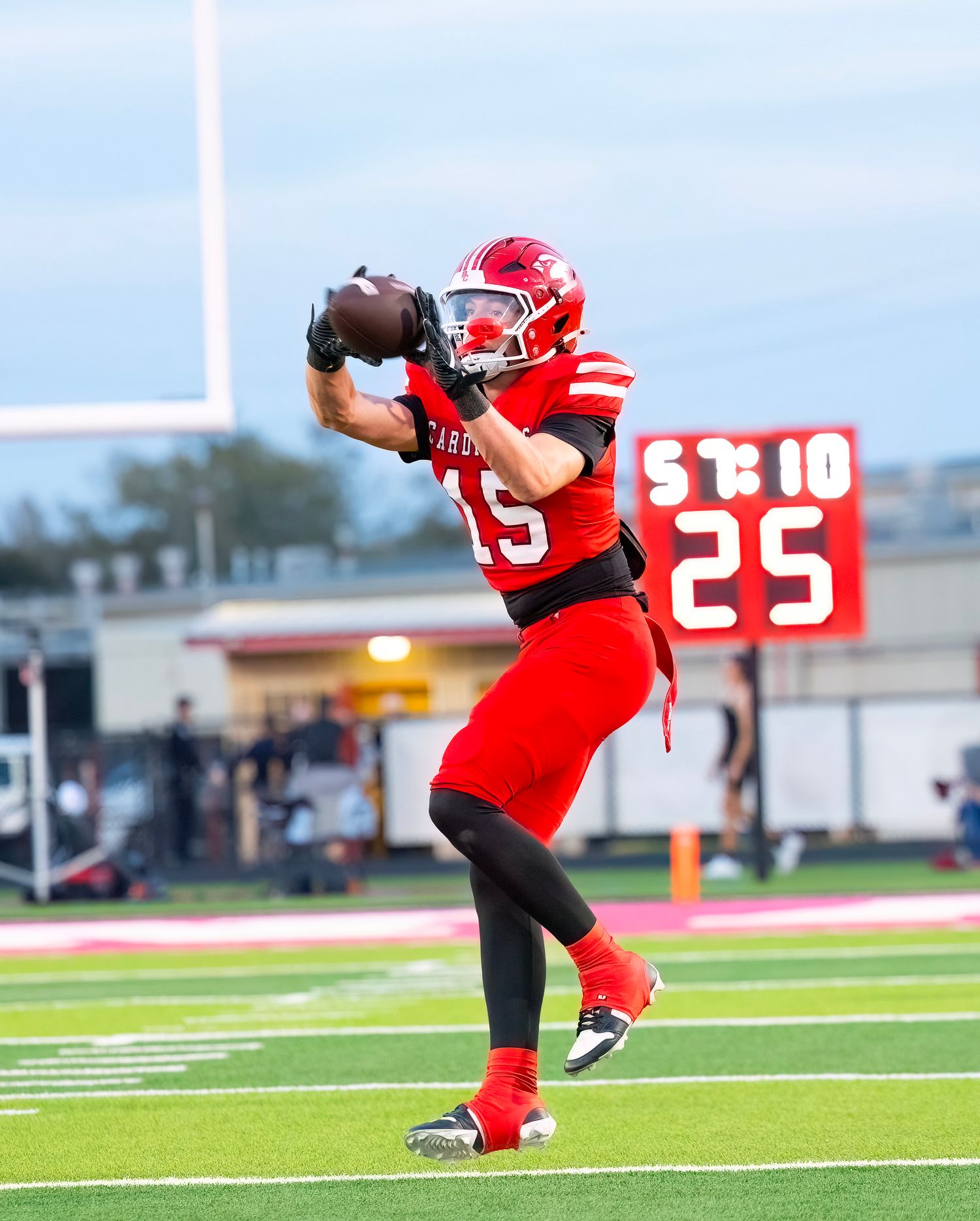 Football player in red uniform practices punting technique on field during daytime.