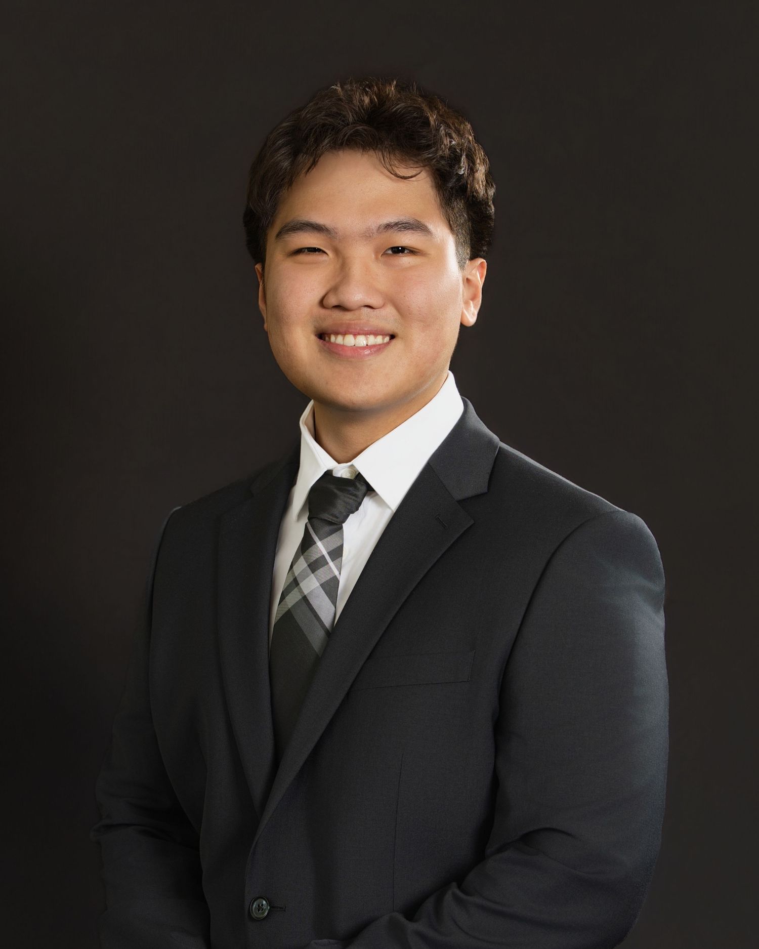 Professional studio portrait of someone in a black suit and striped tie against a dark background.