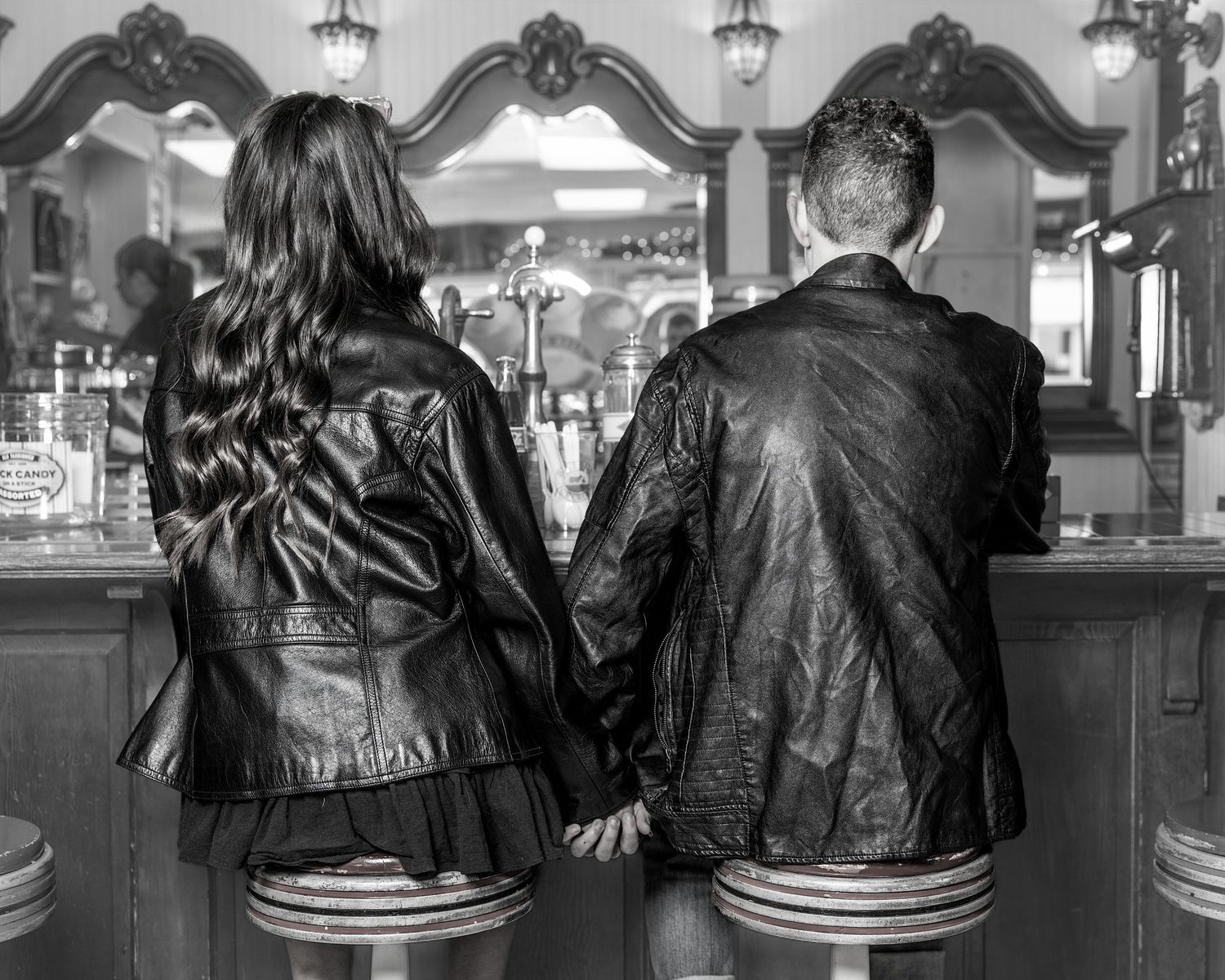 Black and white photo of couple in leather jackets sitting at vintage diner counter.