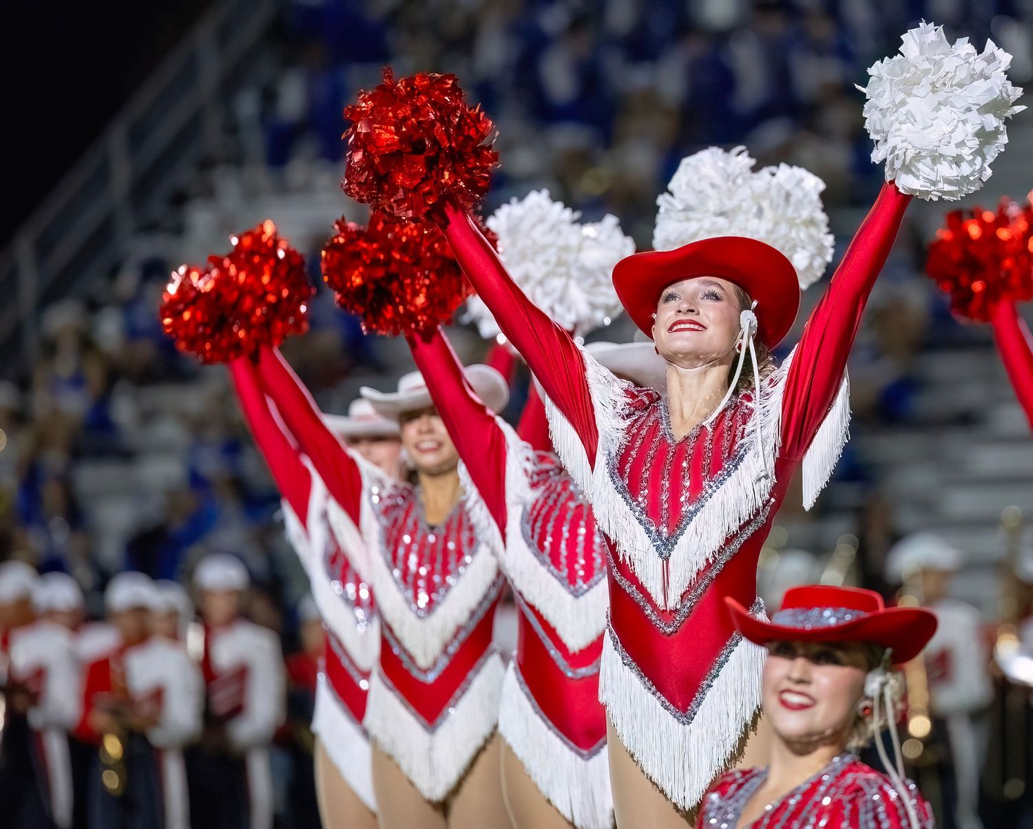 Bridge City Strutters in sparkly red and white uniforms with cowboy hats perform during a sporting event.