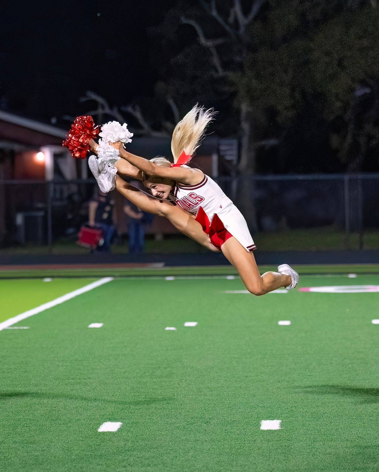 Cheerleader performs an impressive horizontal aerial flip on the football field at night.