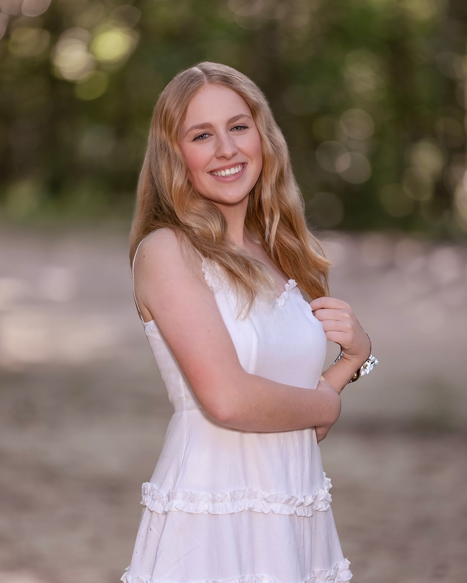 A person in a white ruffled dress poses outdoors with a soft bokeh background during golden hour.