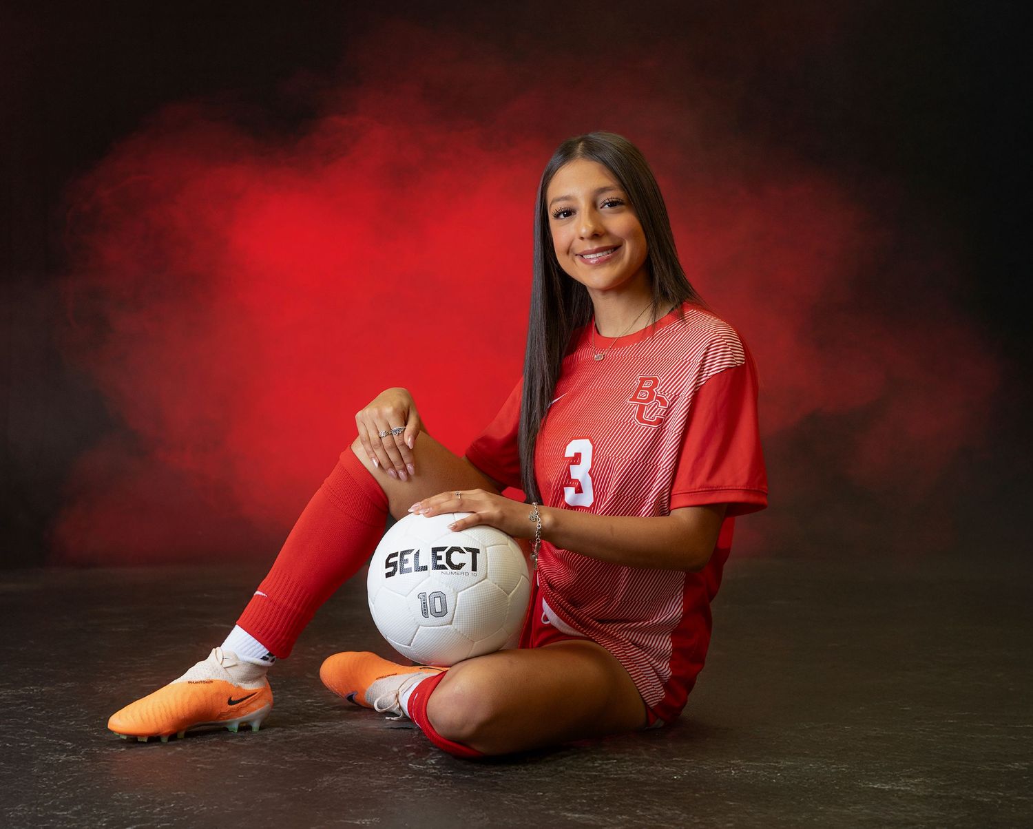 Soccer player in red uniform poses with white ball against dark background in creative photo series.