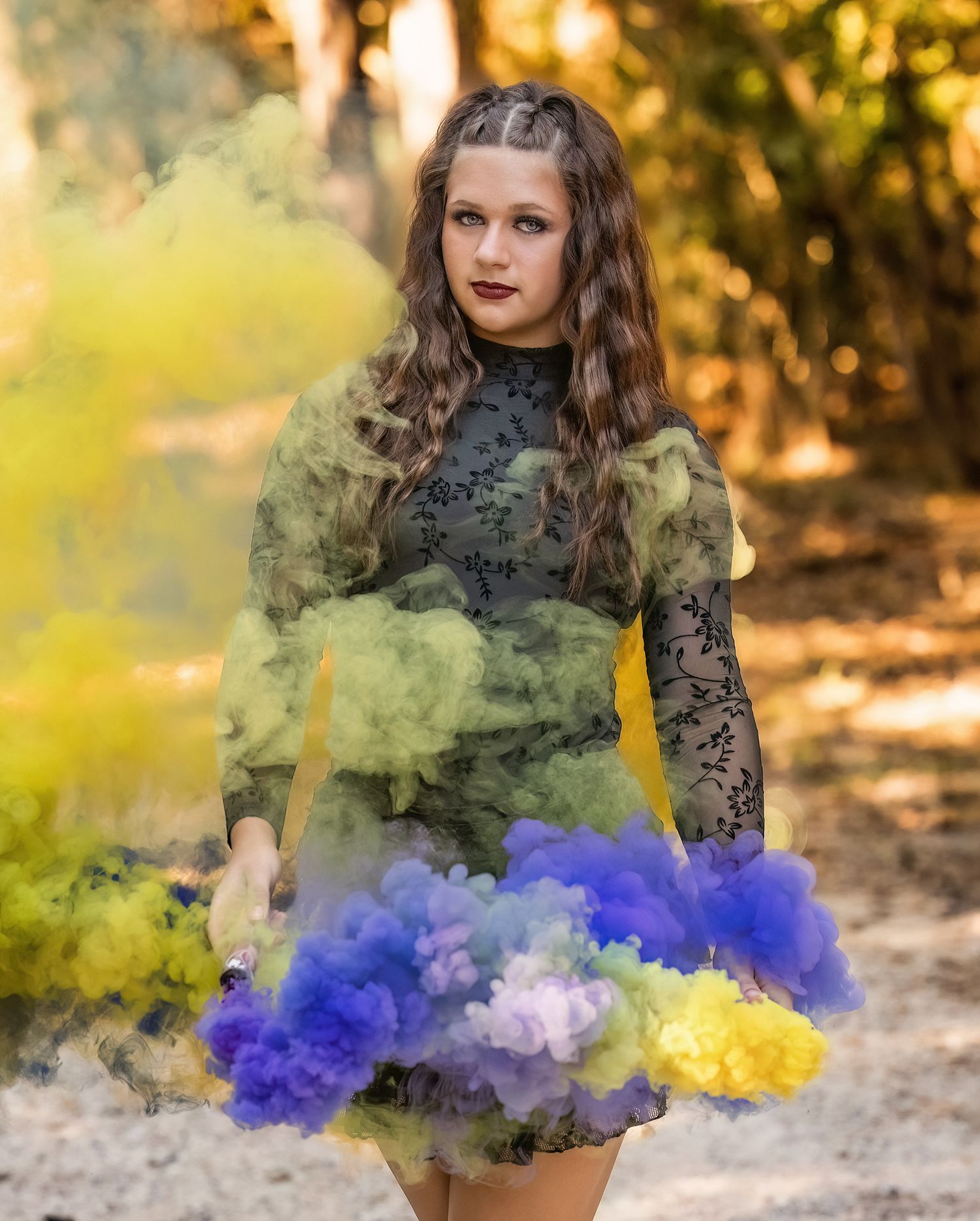 Artistic portrait with colorful yellow and blue smoke effects in an autumn forest setting.