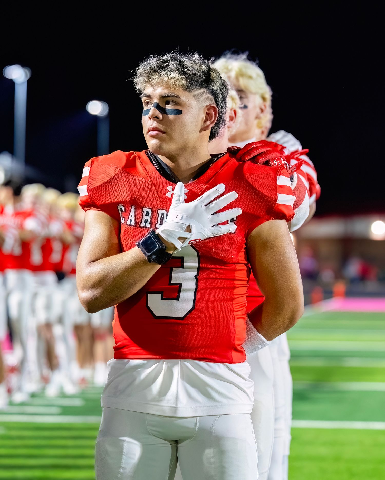 Football players in red and white uniforms stand on field during nighttime game.