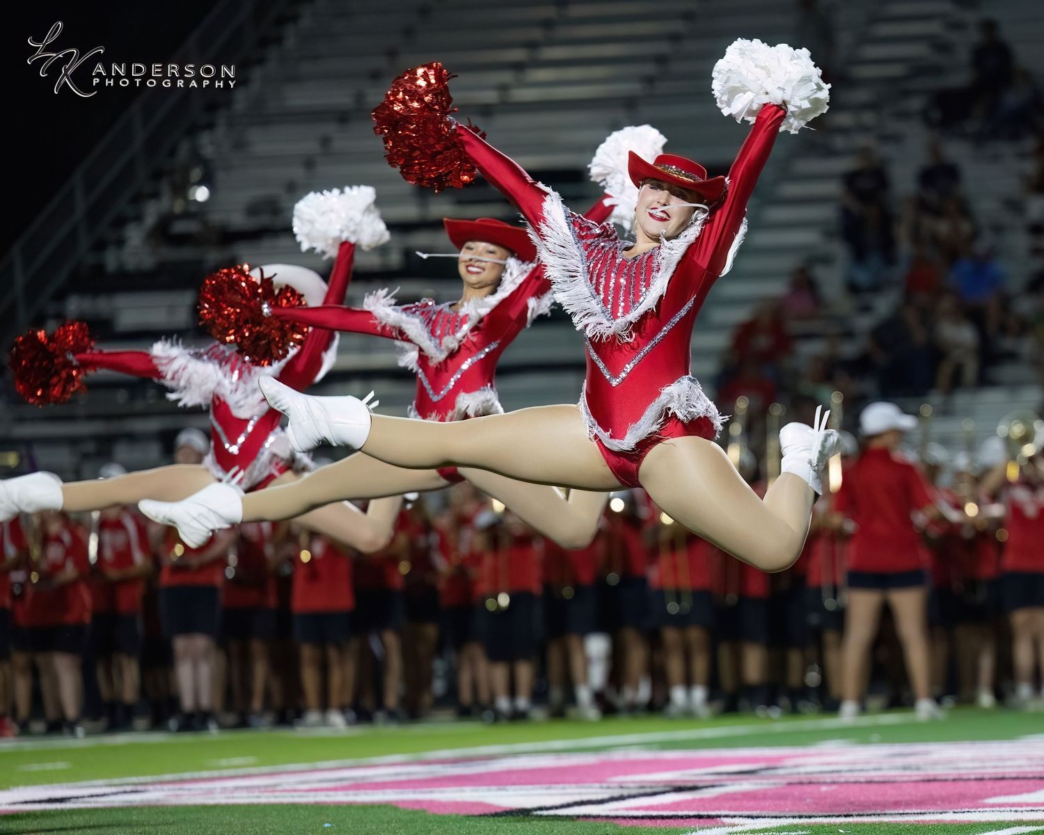 Dancers execute a synchronized aerial move in red and white uniforms on a football field.