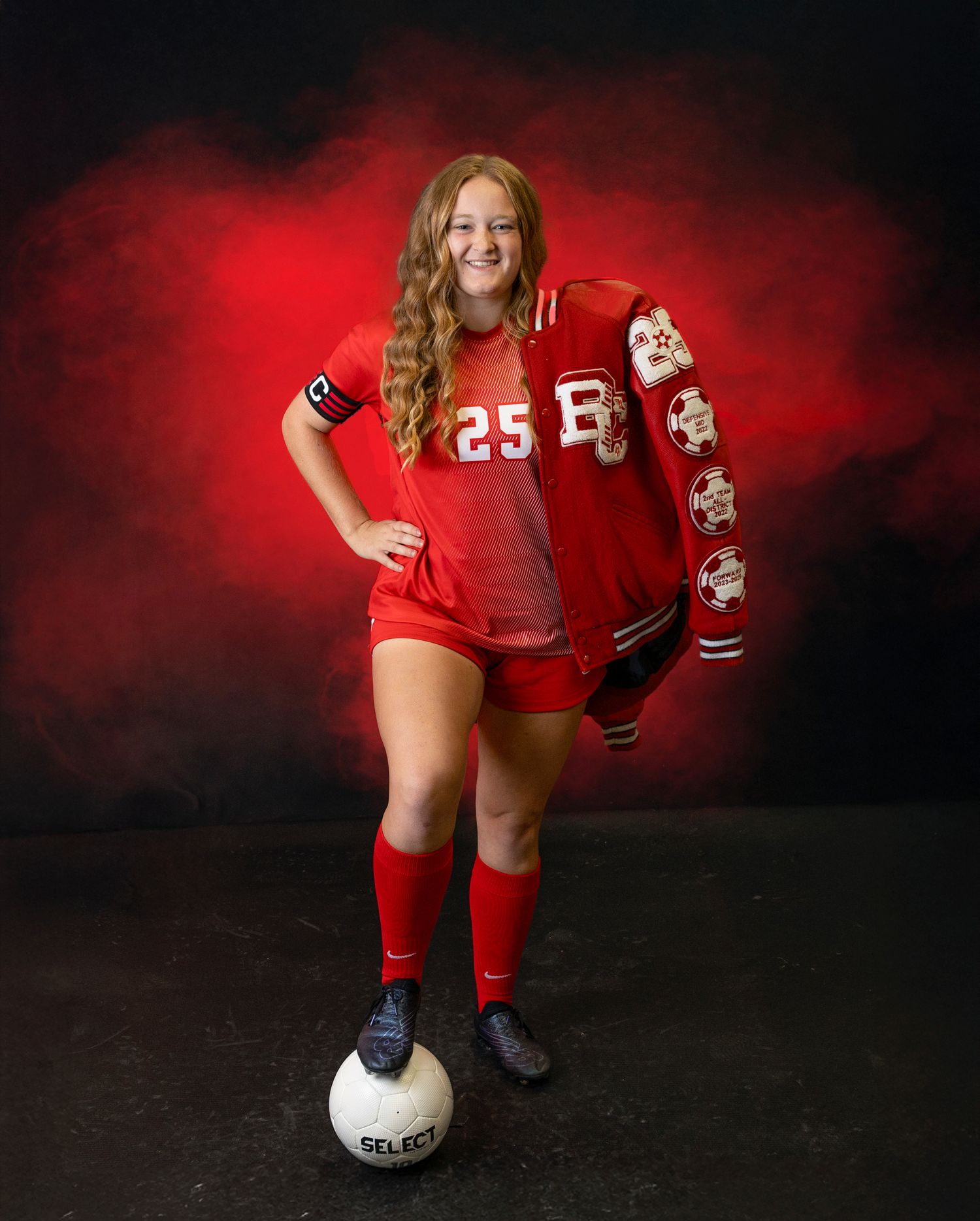 Volleyball player in red uniform poses with ball against dramatic red and black backdrop.