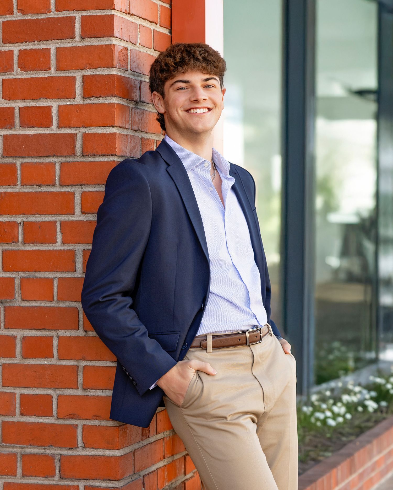 Young graduate in navy blazer and khakis poses against brick wall for professional portraits in outdoor setting.