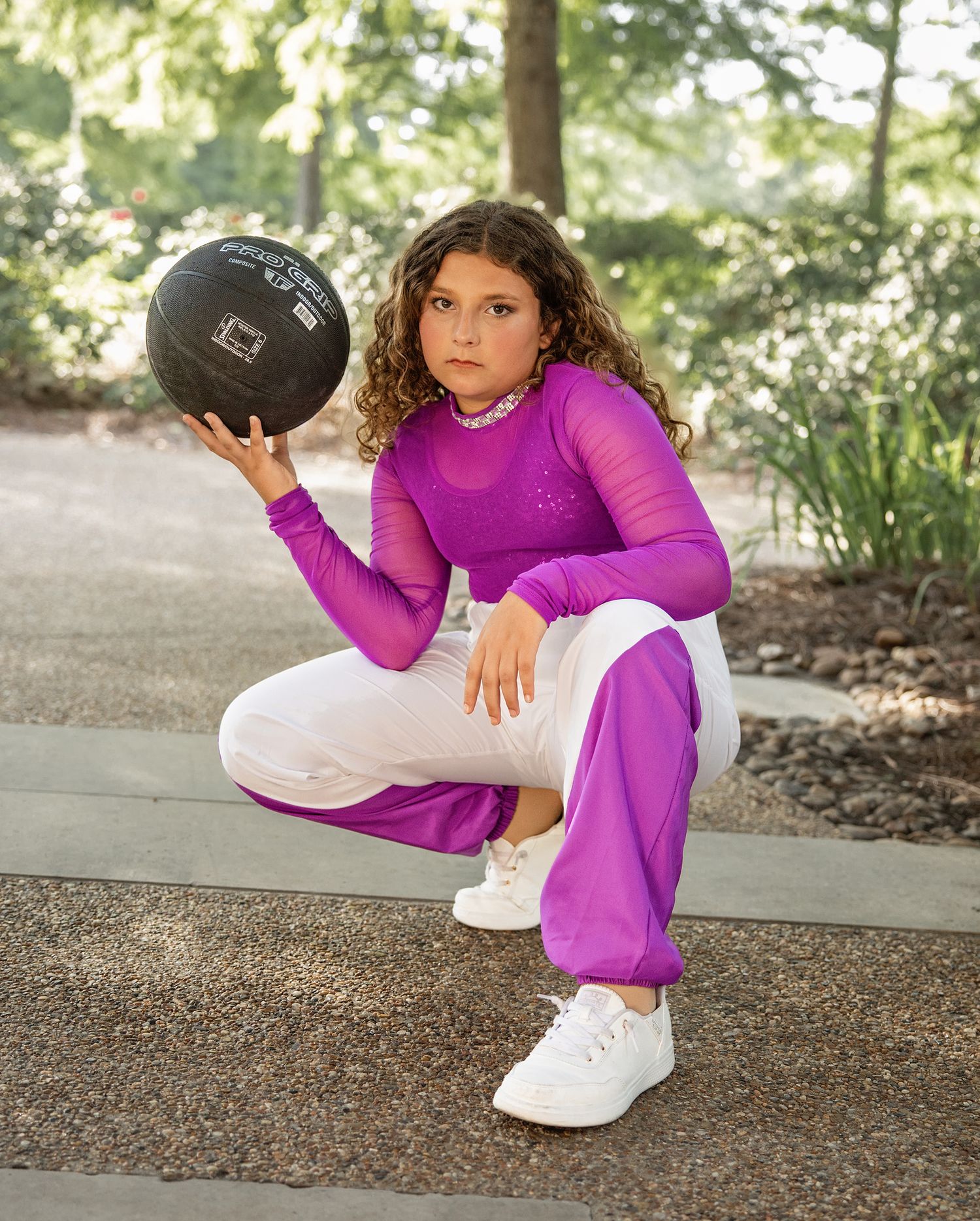 Teen photoshoot in a purple athletic outfit and white sneakers demonstrates a dynamic stretching pose outdoors.