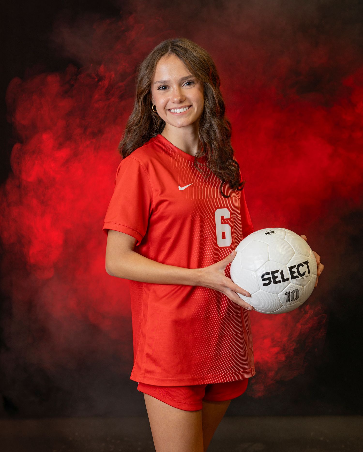Athletic figure in red jersey poses with volleyball against dramatic red and black backdrop for sports portrait series.