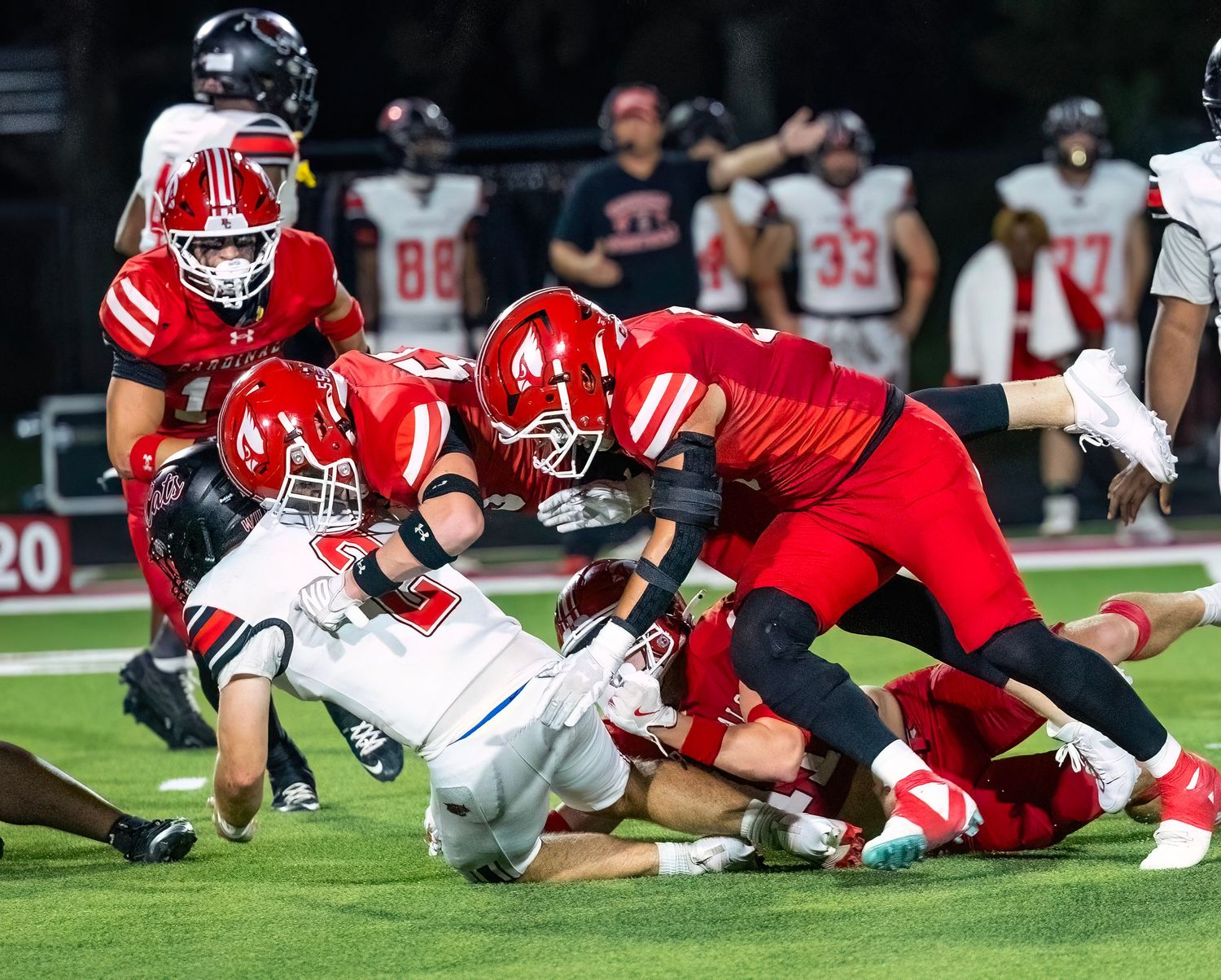 Football players dive for a loose ball during an intense game between teams in red and white uniforms.