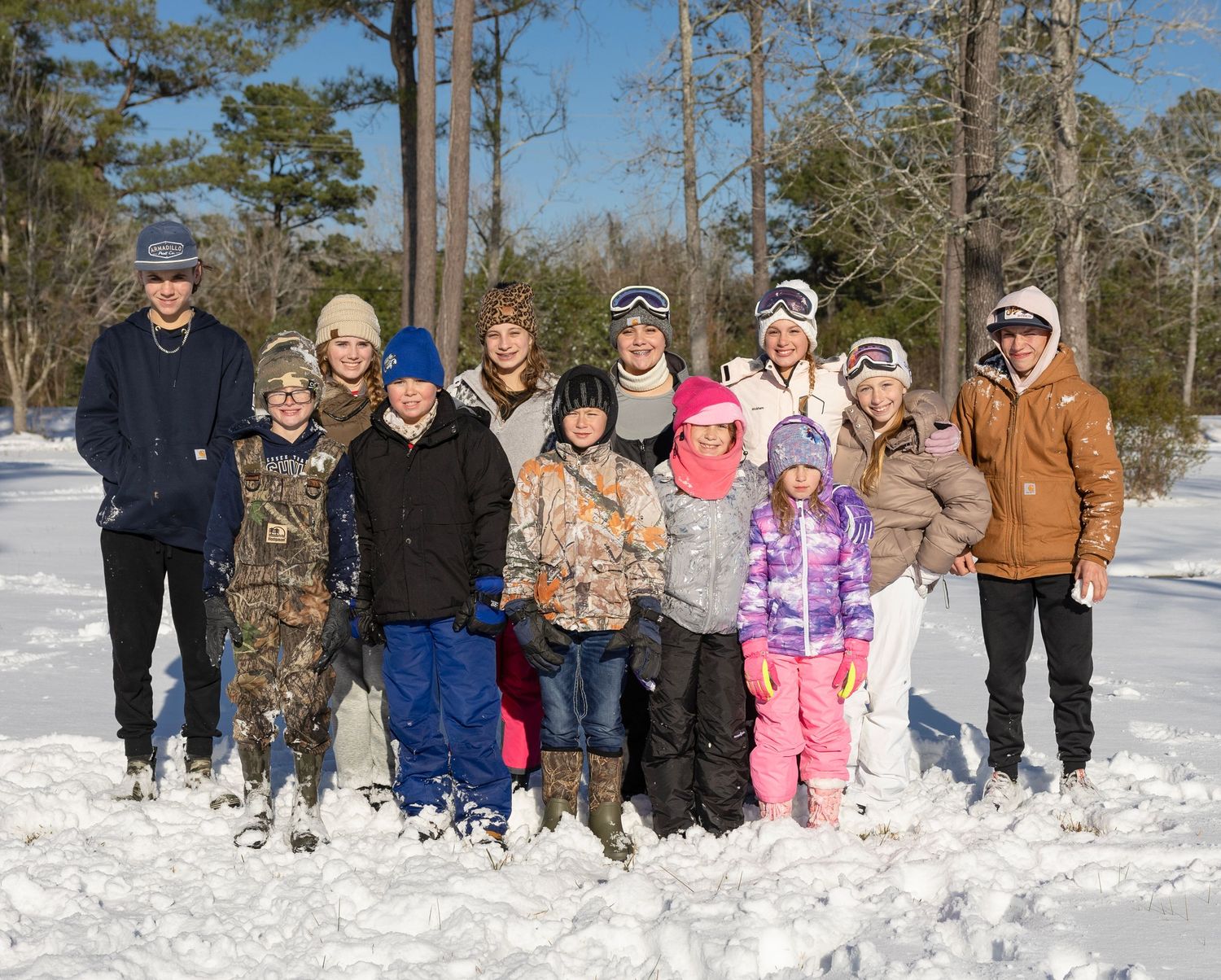 Snow Event Group of people enjoying a winter day in the snow surrounded by tall pine trees and white snow-covered ground.