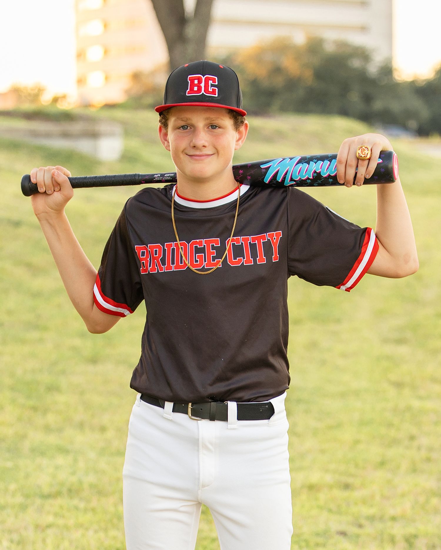 Baseball player in black Bridge City uniform holds bat on sunny field.