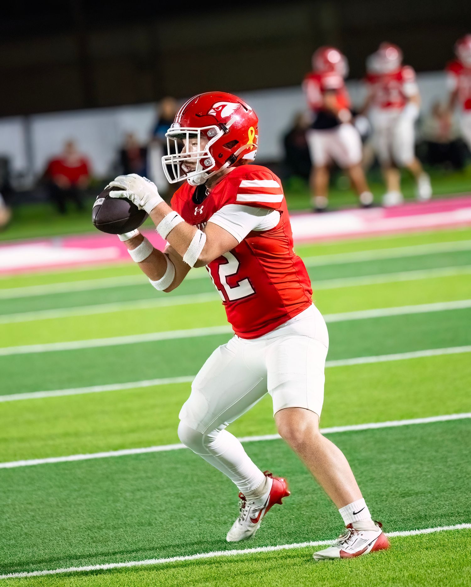 Athletes in red and white uniforms perform synchronized stretching exercises on a green football field.