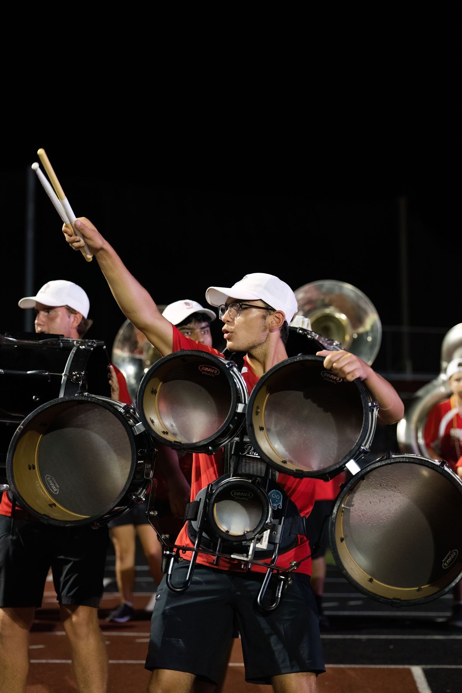 Marching band performers hold large cymbals in a synchronized formation during a nighttime performance.