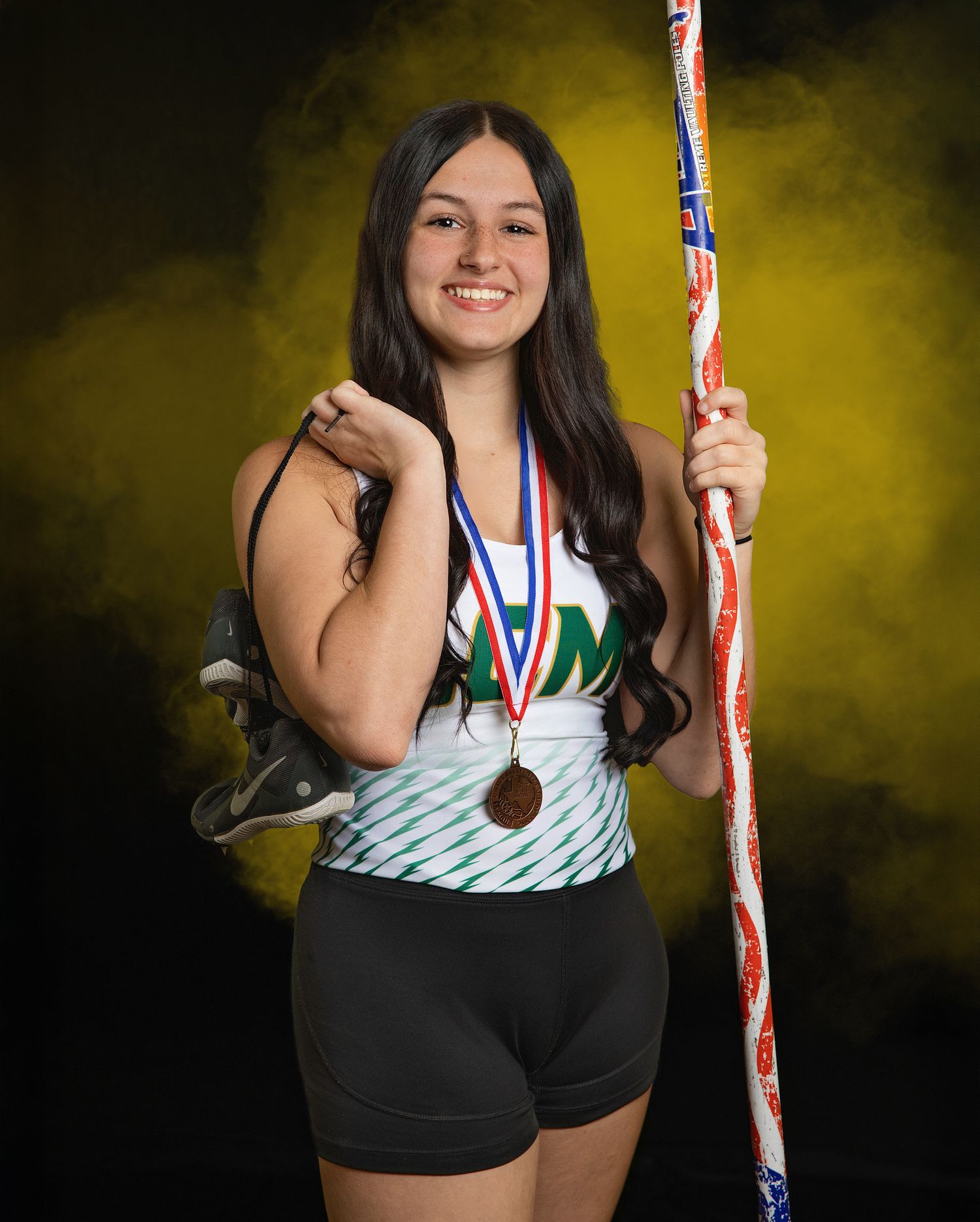 Athlete poses with medals and sports equipment against dramatic yellow backdrop in professional studio portraits.