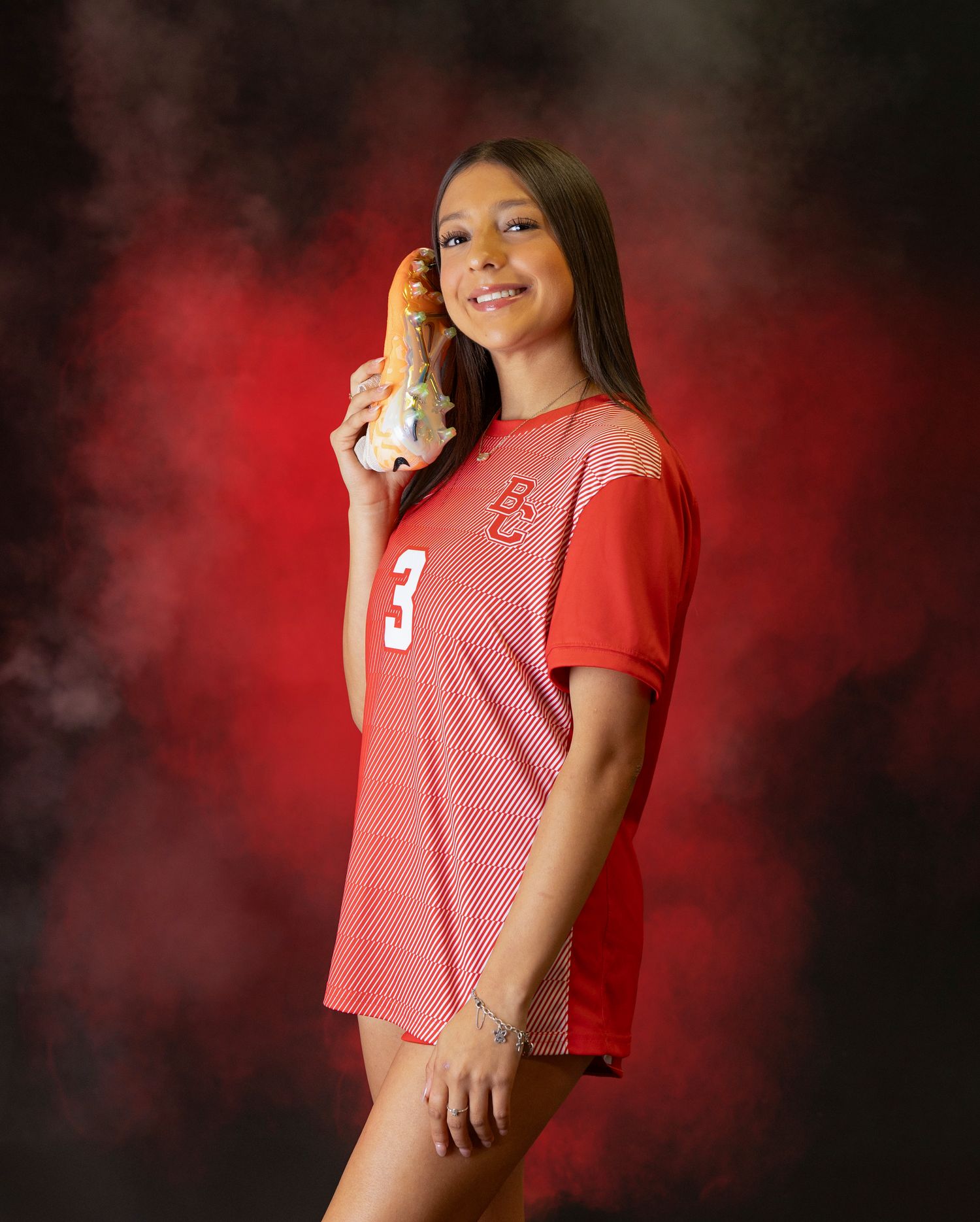 Athletic portrait of someone in a red mesh jersey number 3 against a dramatic red smoky background.