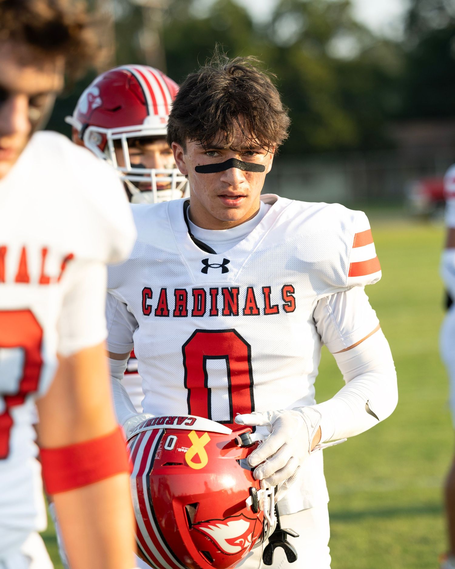 High school football players in white Cardinals uniforms gather on the field during a game.