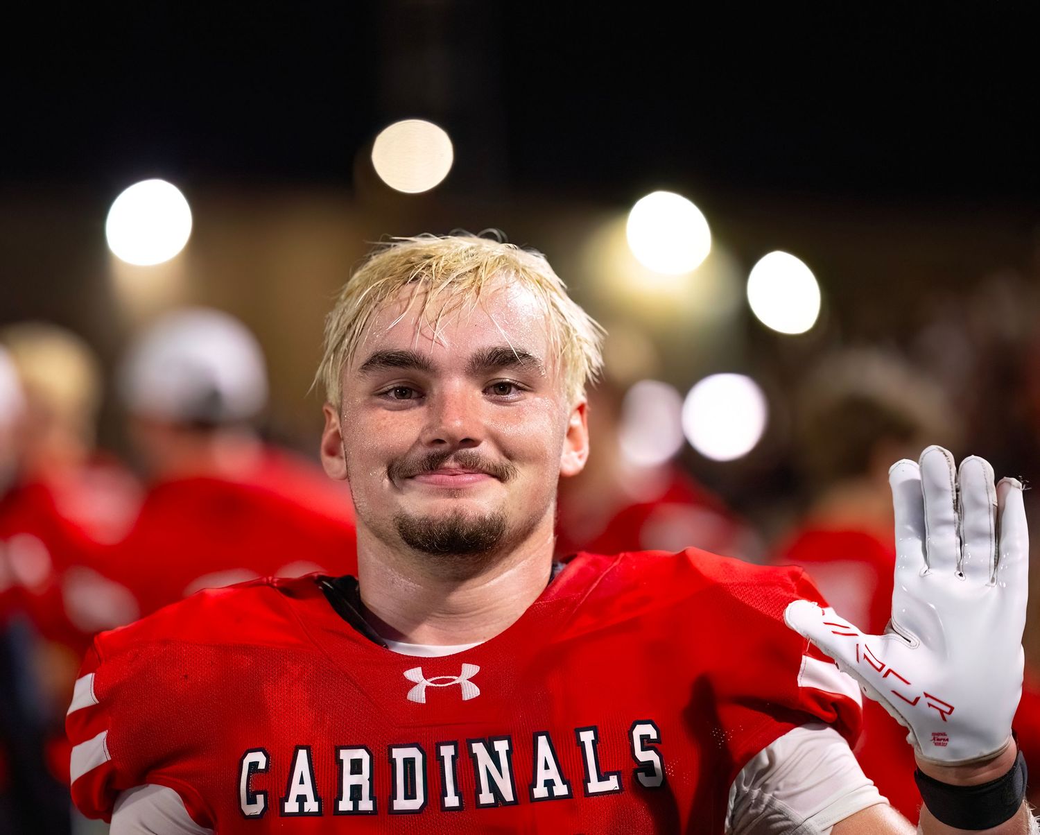 Cardinals football players celebrating under stadium lights during a night game.