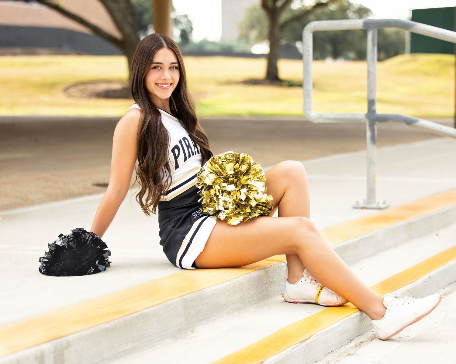 VHS Cheerleader Laney in black and white uniform poses with gold pom poms on outdoor steps.