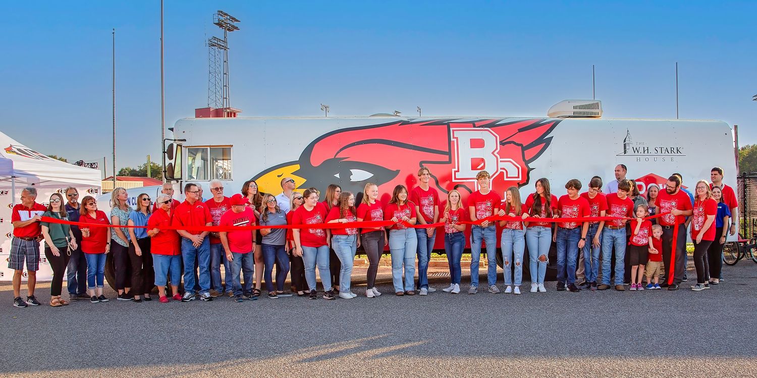 Bridge CTE Stem Bus ribbon cutting of people wearing red shirts gathered in front of a red helicopter at an outdoor event.