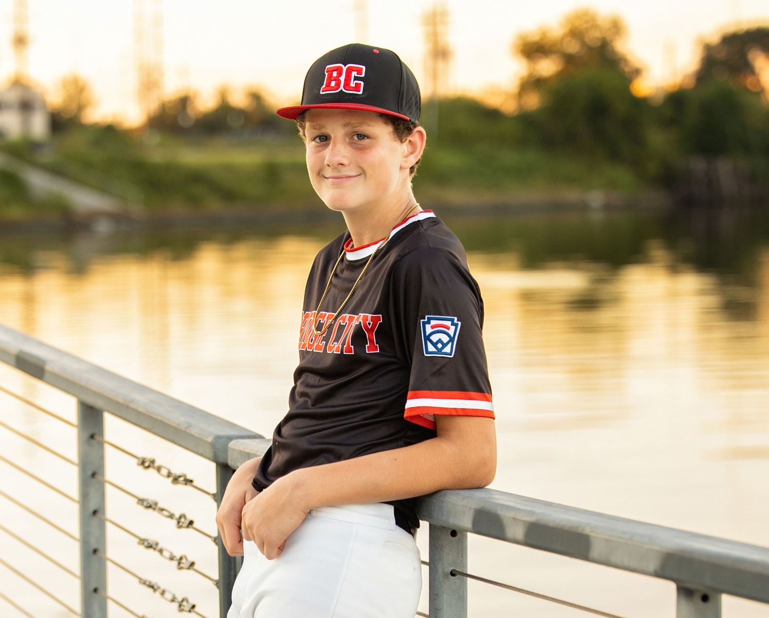 A person wearing a baseball cap sits on a wooden dock by a serene lake at sunset.