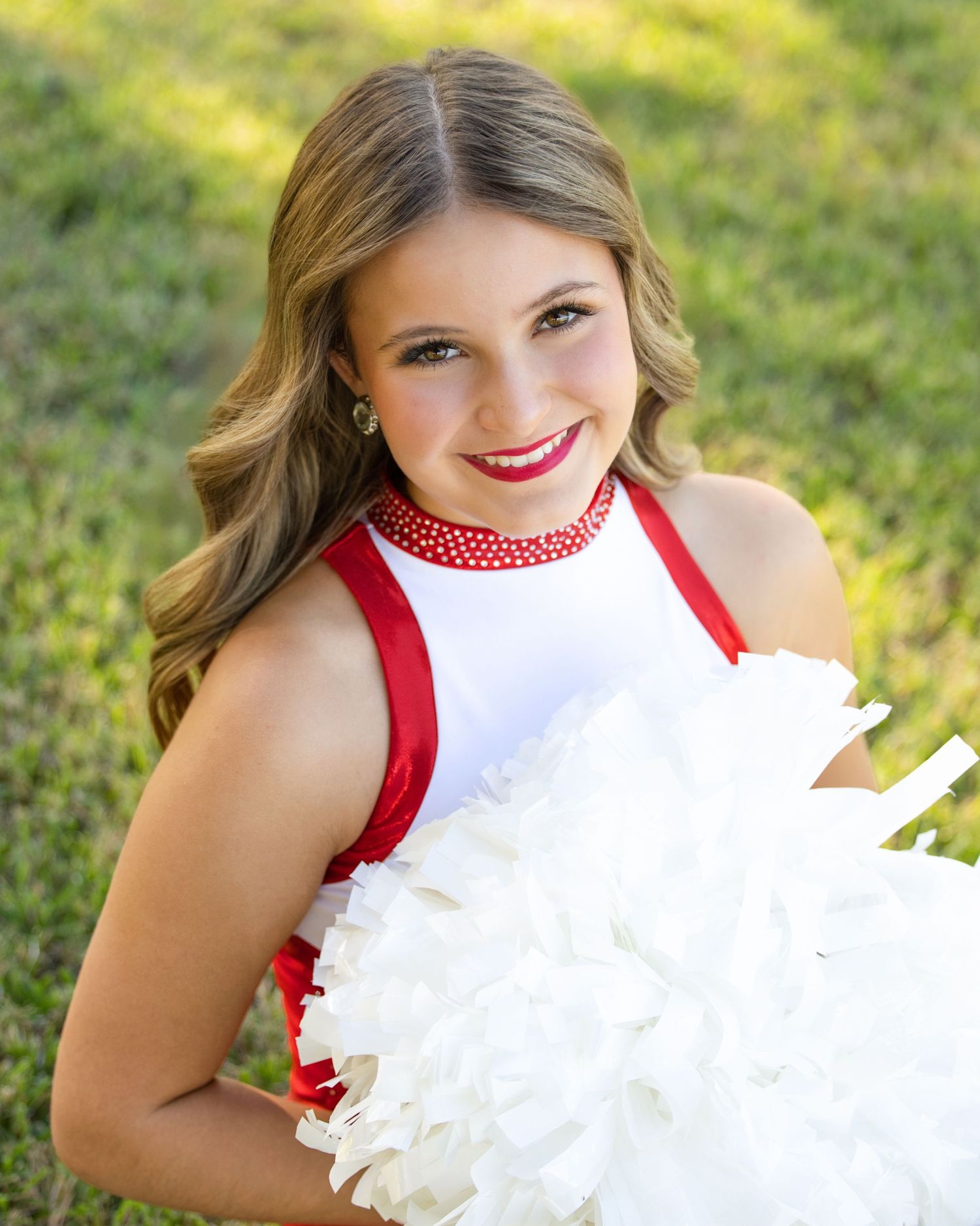 White and red cheerleading uniform with decorative pom poms against green grass background.