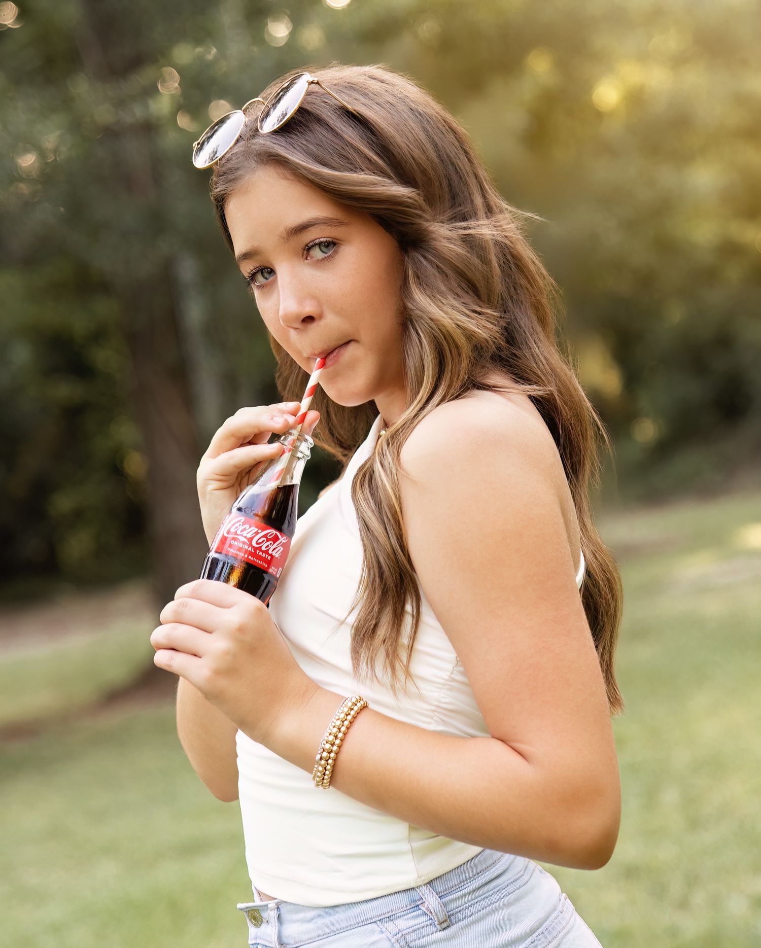 Summer portrait session showing someone in casual attire drinking from a glass bottle in warm sunlight.
