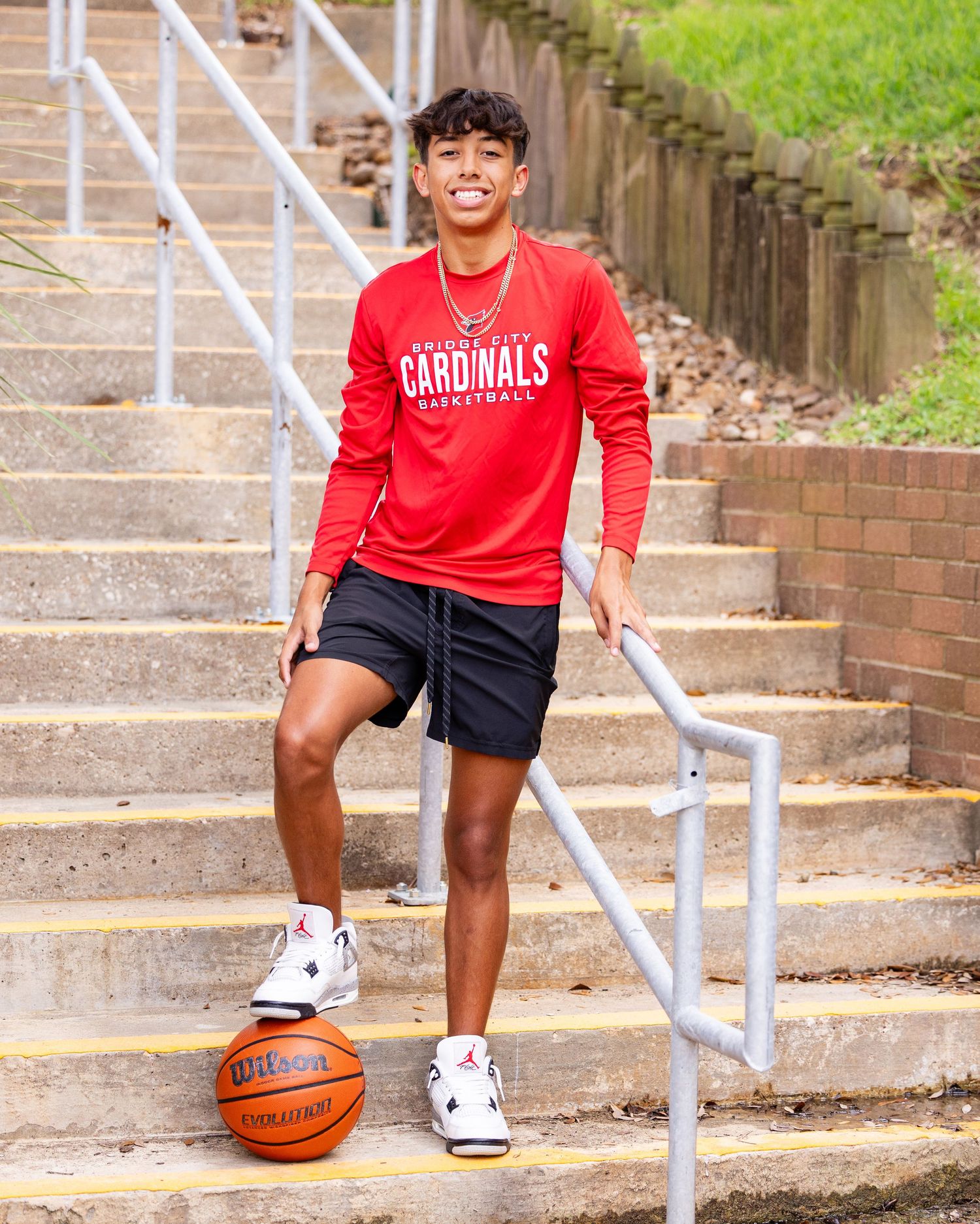 Basketball player in red Cardinals jersey sits on brick steps with ball showing athletic spirit.