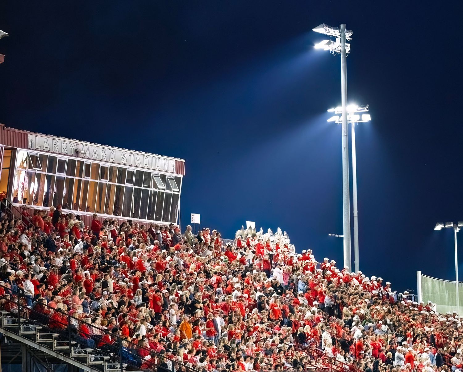 Panoramic view of crowded stadium bleachers filled with fans wearing red under bright night lights.