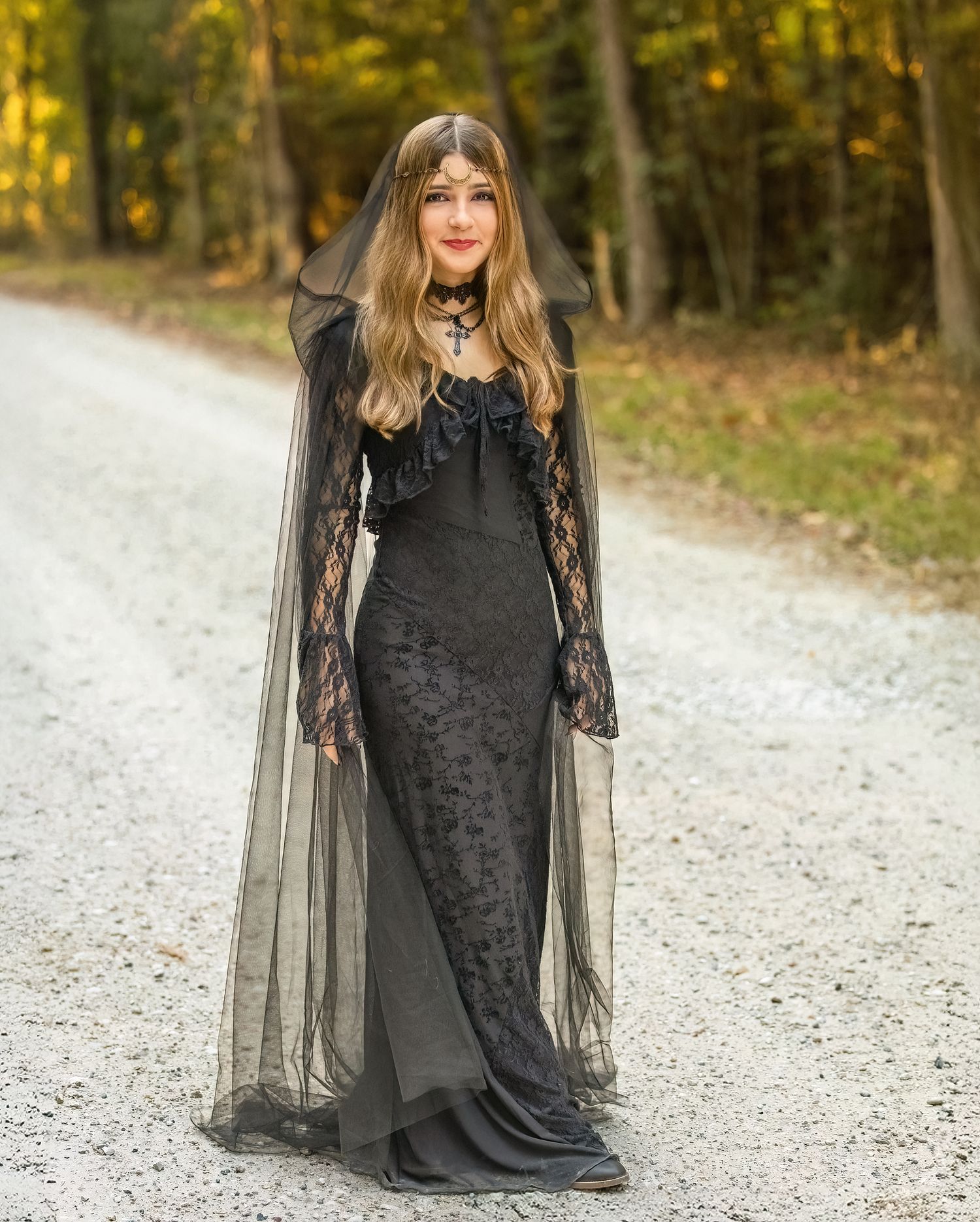 Gothic-inspired photo on a forest path featuring a long black lace dress and sheer cape.