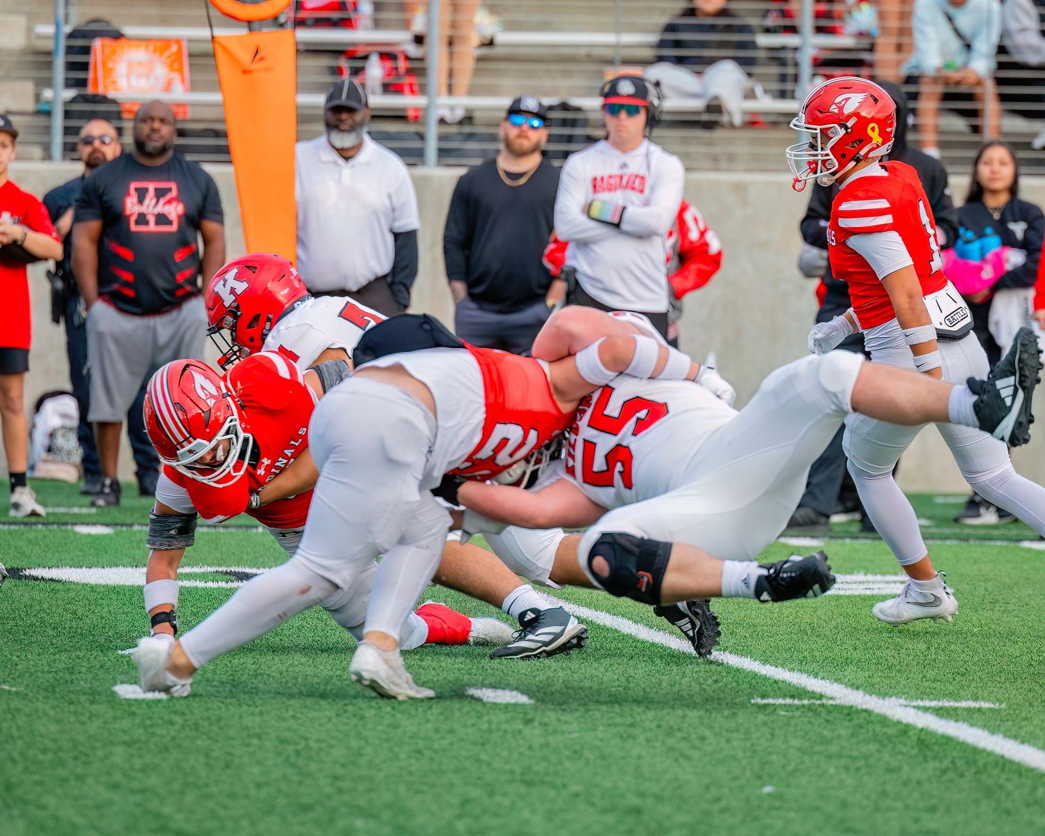 Football players execute blocking positions during practice drill on artificial turf field.