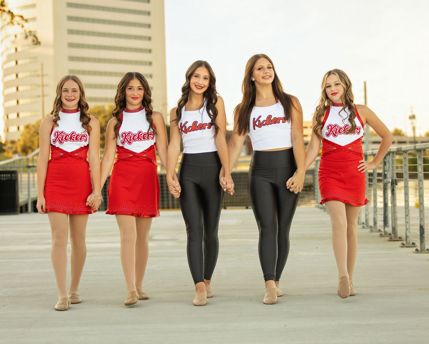 A group of cheerleaders in red and white uniforms walking together in a line along a waterfront path.