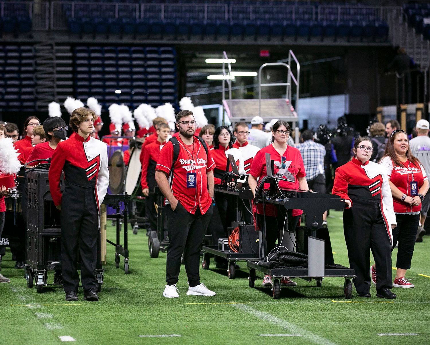 Bridge City Marching band members in red and black uniforms perform in formation on a grass field during a performance.