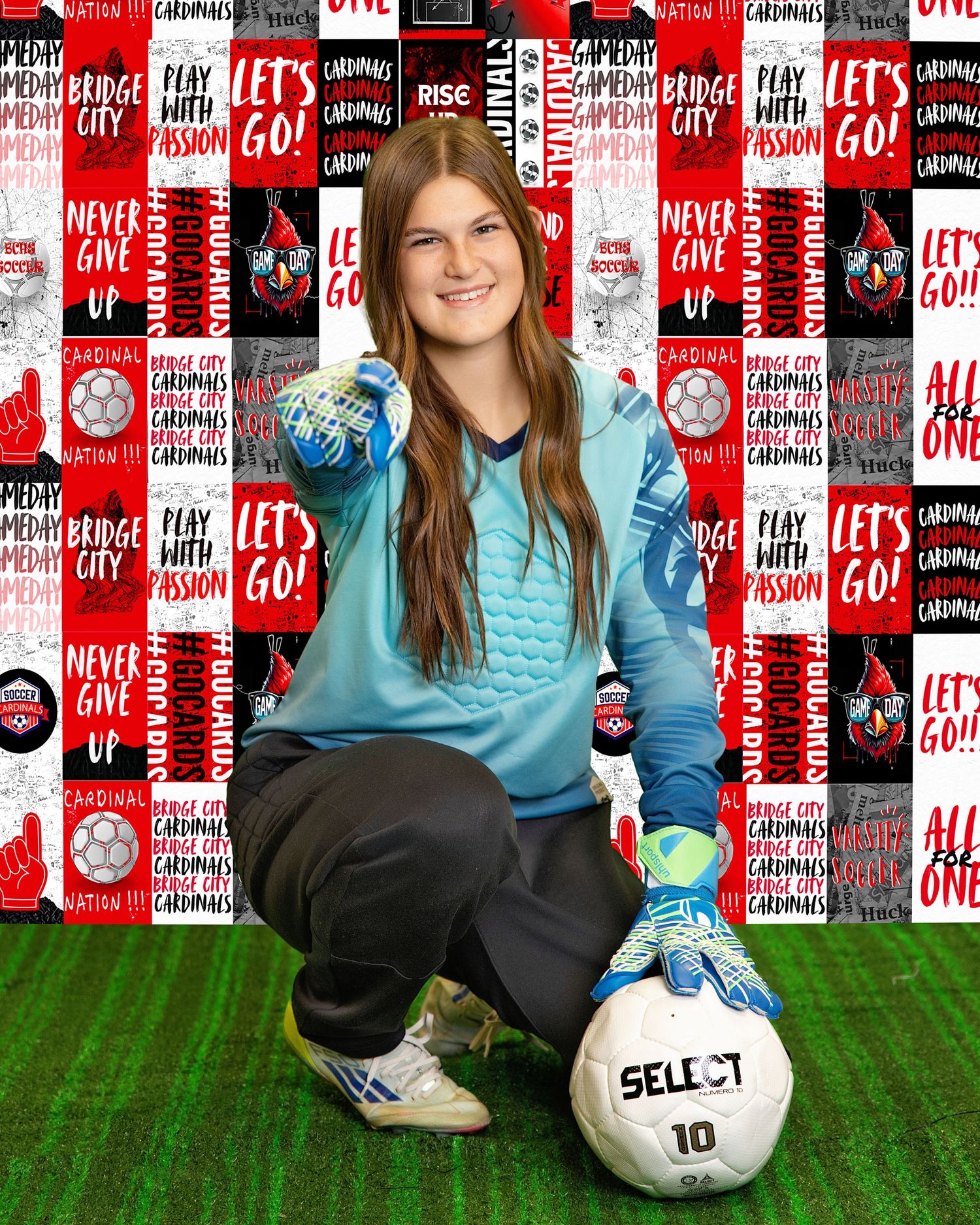 Soccer player in blue shirt and black pants poses with ball on artificial turf against red and white backdrop.